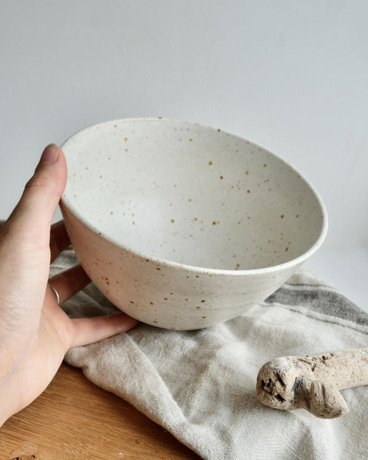 Hand holding a speckled ceramic bowl on a light gray surface with a wooden edge.