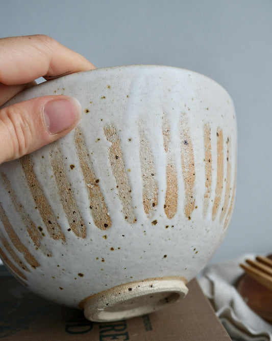 Hand holding a white ceramic bowl with a textured surface against a neutral background