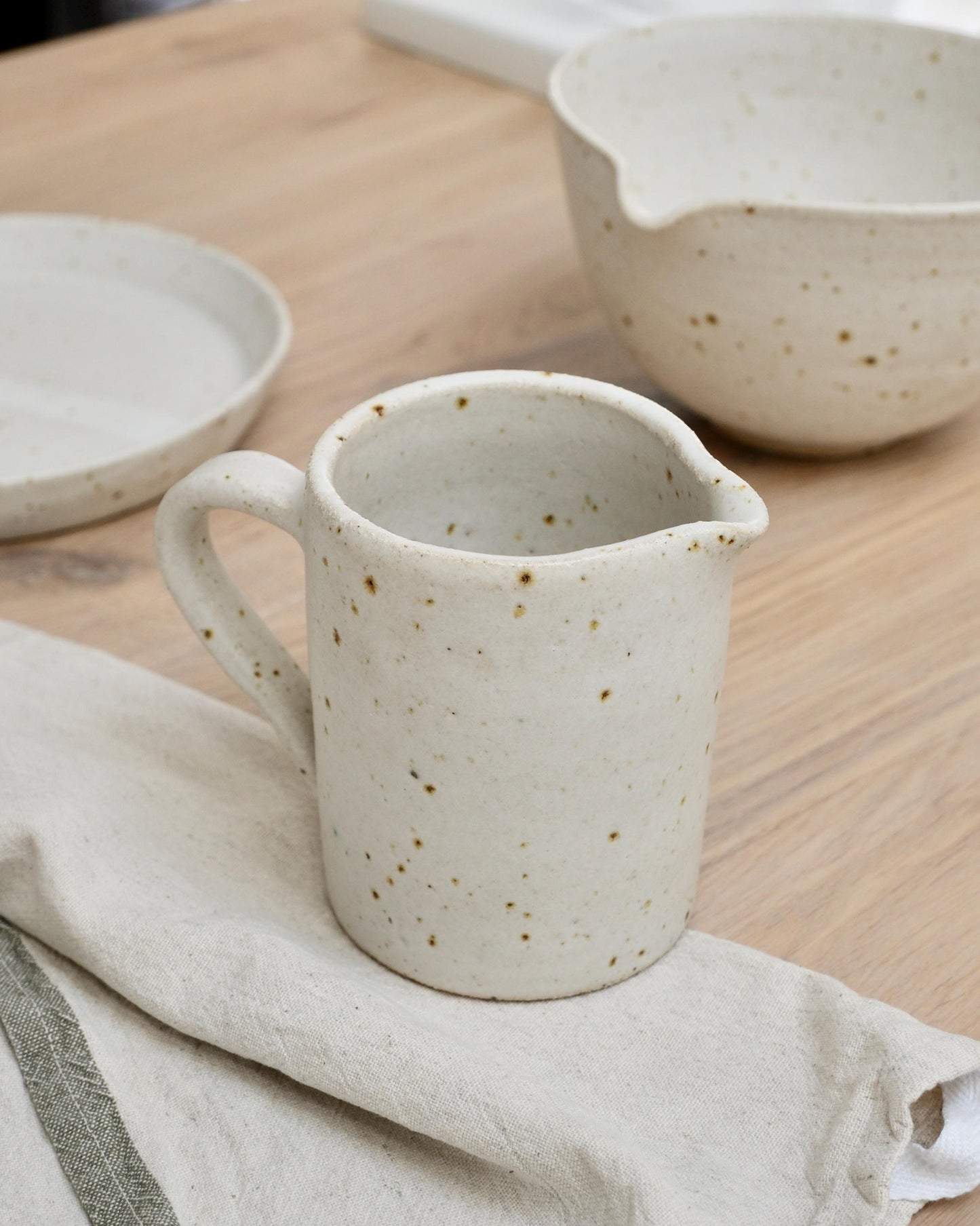 White speckled ceramic milk jug on a wooden surface with a cloth underneath