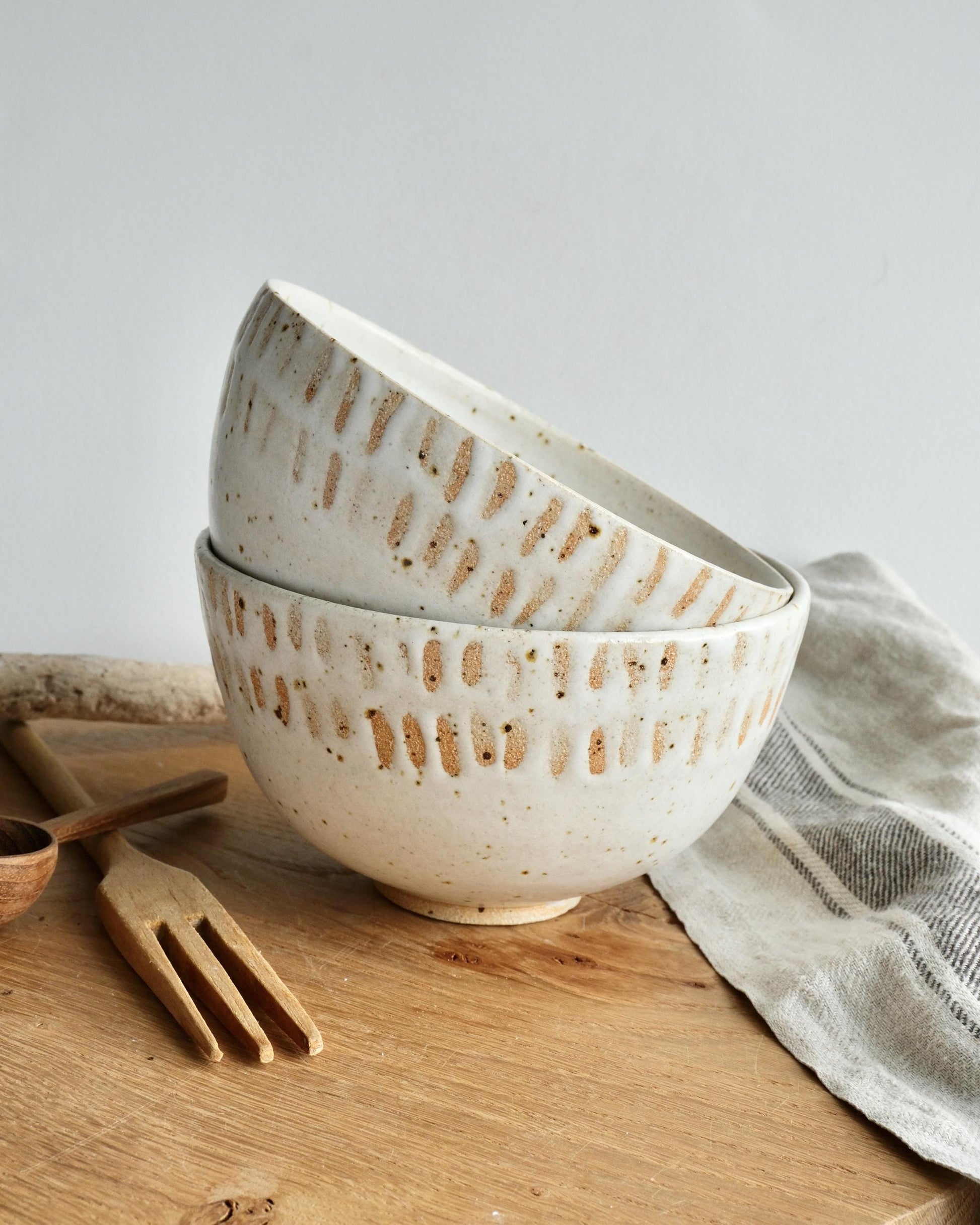 Two white speckled ceramic breakfast bowls with an orange line pattern on a wooden surface with a neutral background