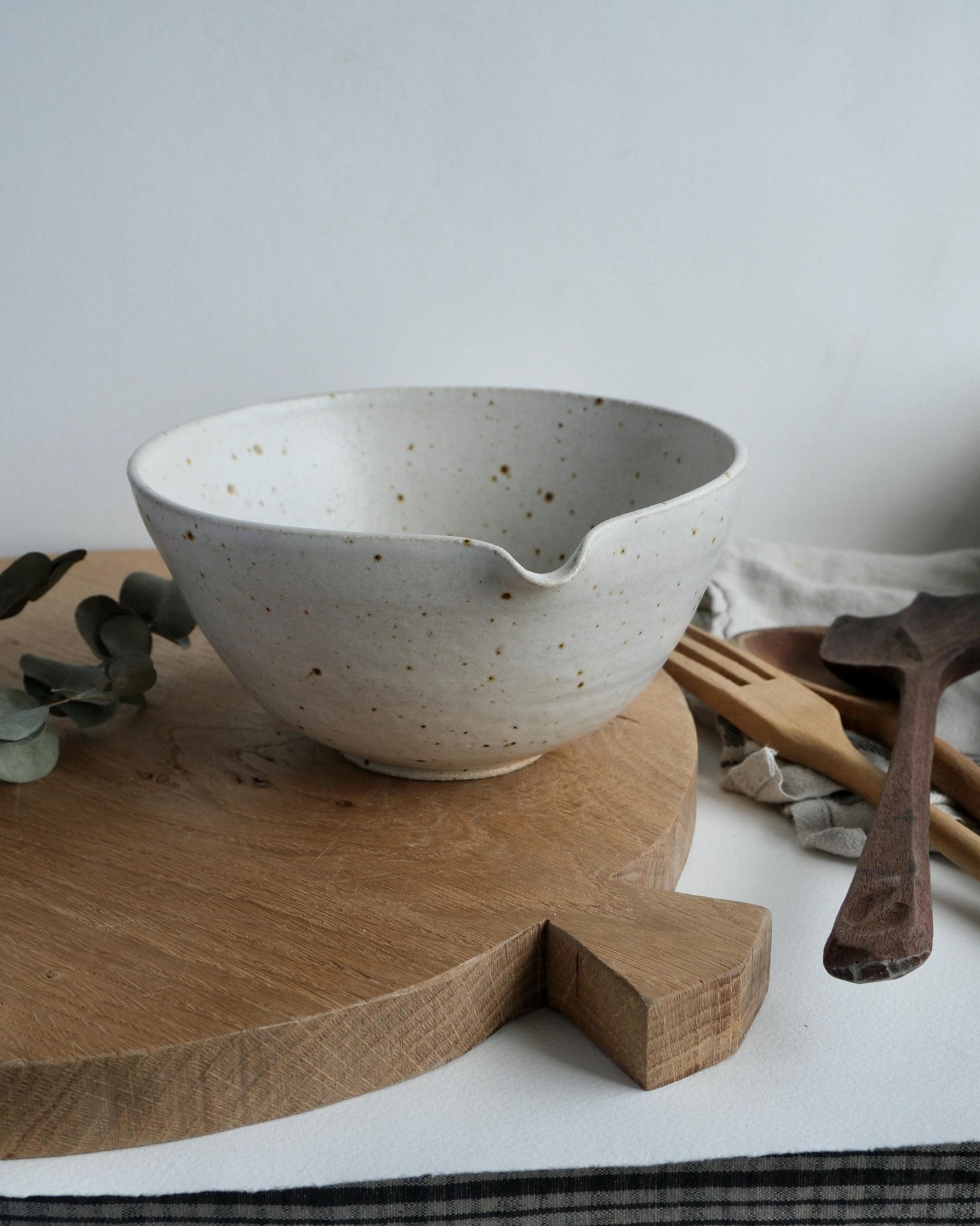 white Speckled ceramic mixing bowl with a pouring spout on a wooden cutting board with a white background