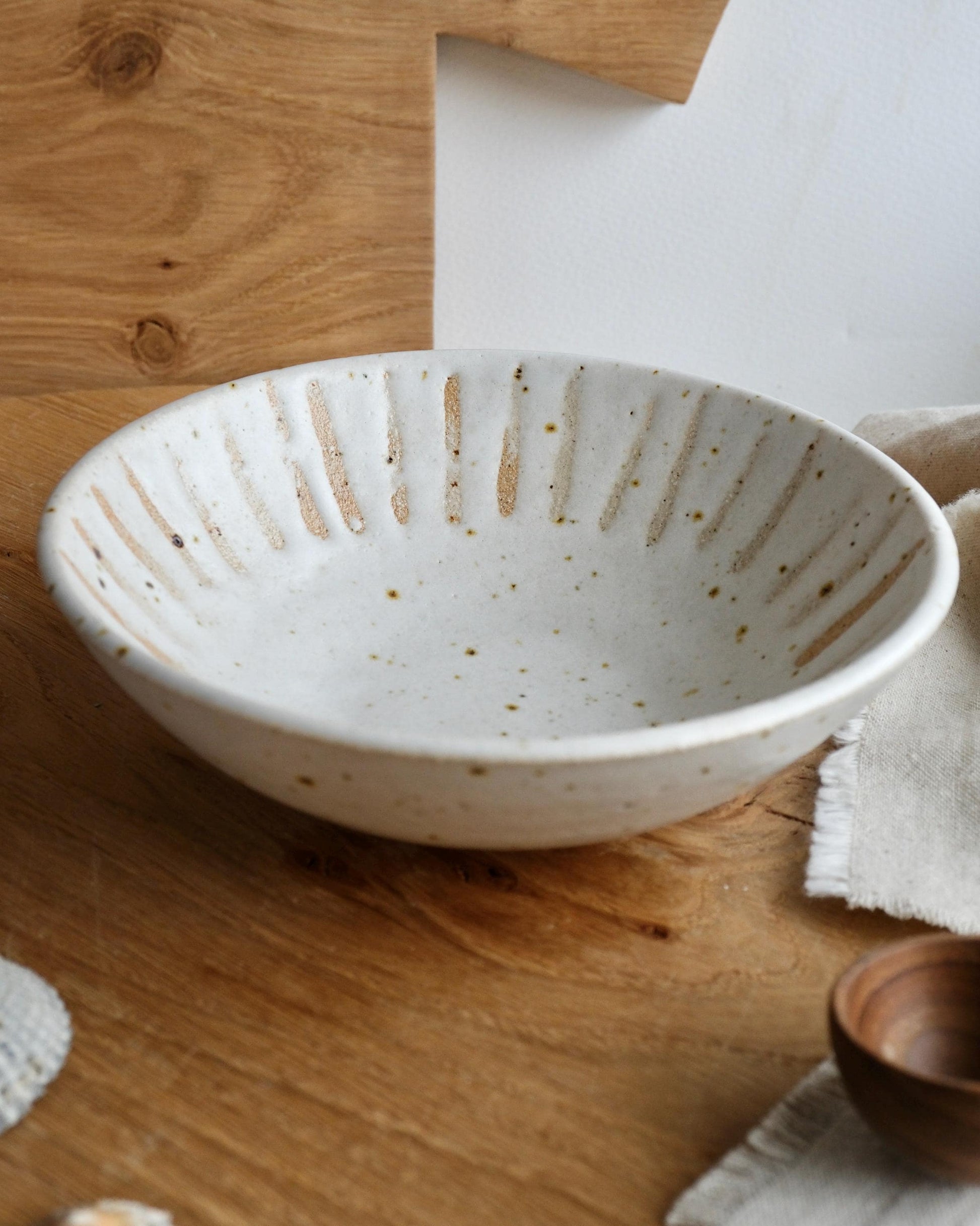 White ceramic bowl with speckled glaze and orange stripe pattern on a wooden surface