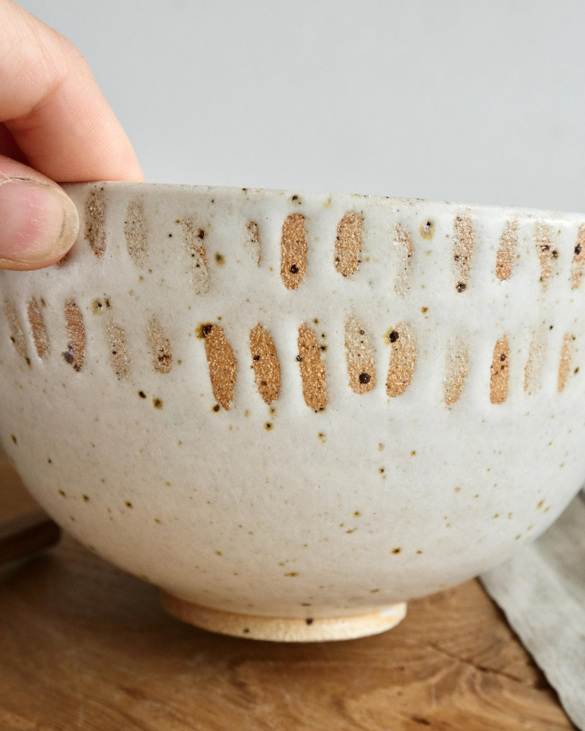 Hand holding a white speckled ceramic bowl with orange line pattern on a wooden surface