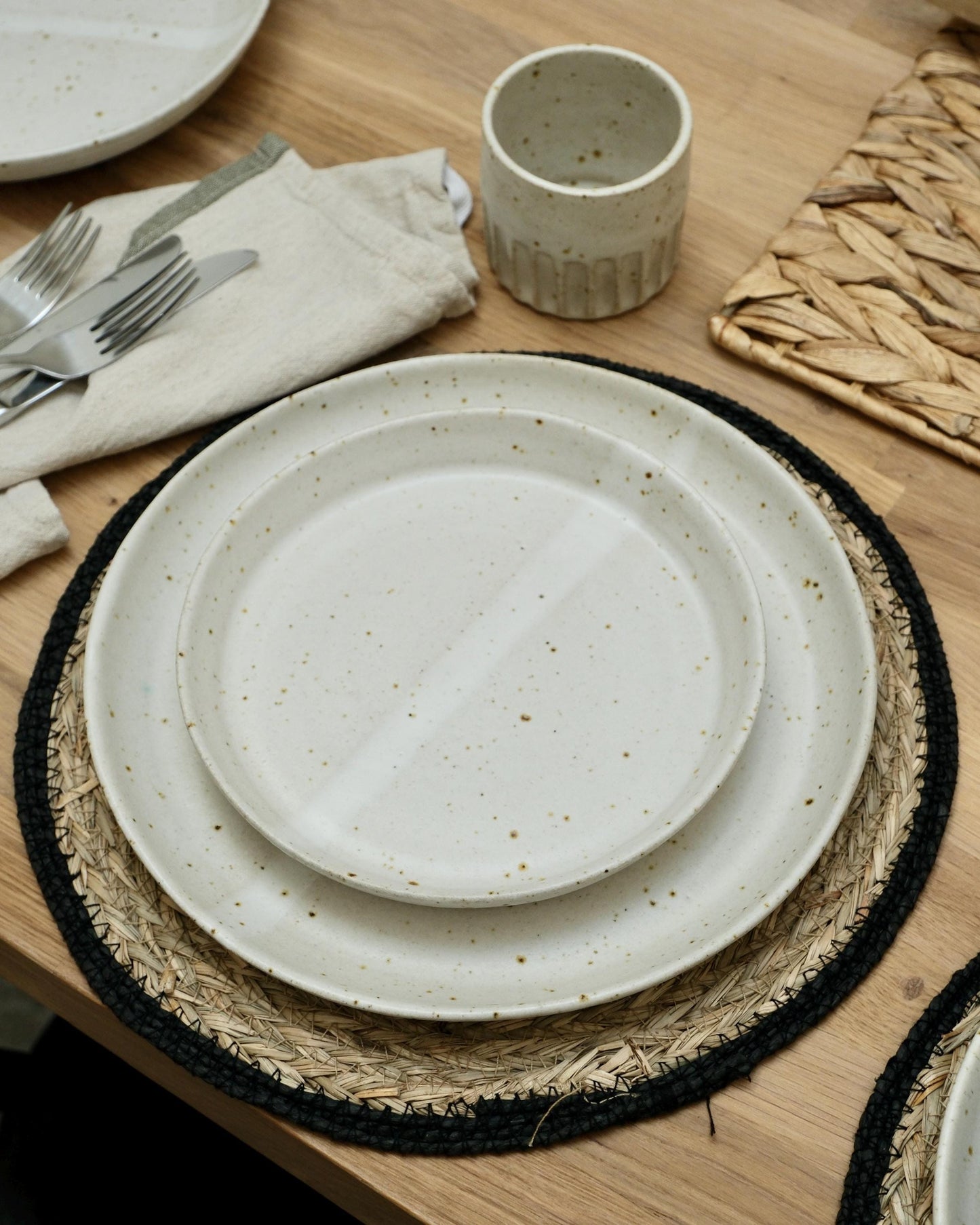 Set of ceramic plates and cups on a wooden table with placemats and cutlery.
