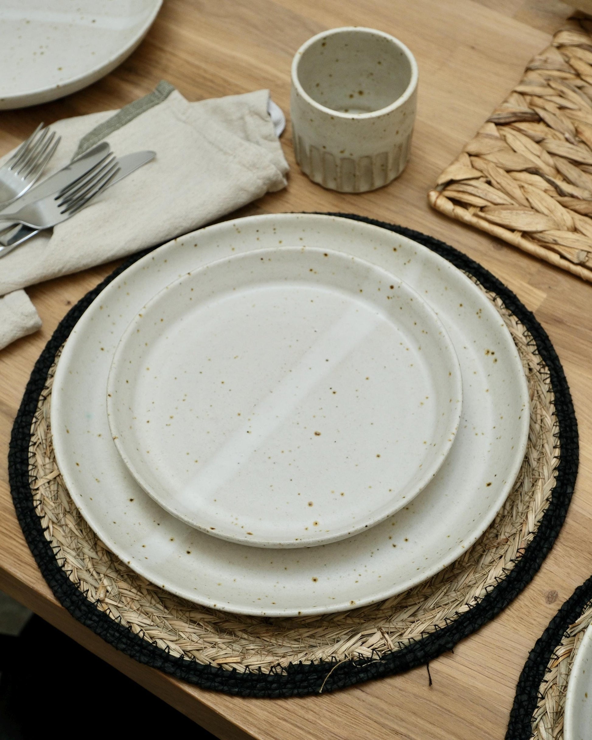 Set of ceramic plates and cups on a wooden table with placemats and cutlery.