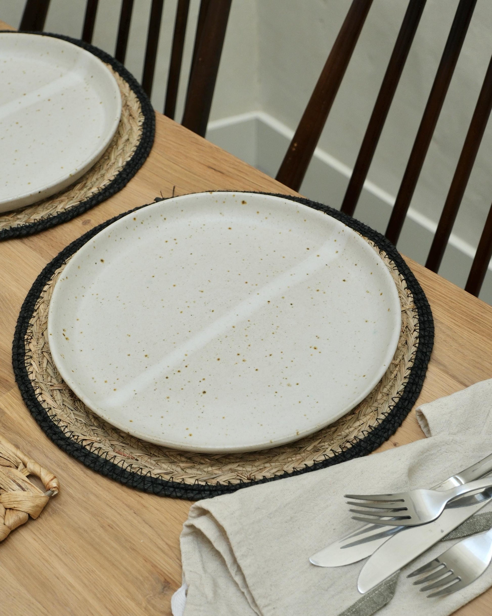 White ceramic plate on a woven placemat with cutlery and napkin on a wooden table.