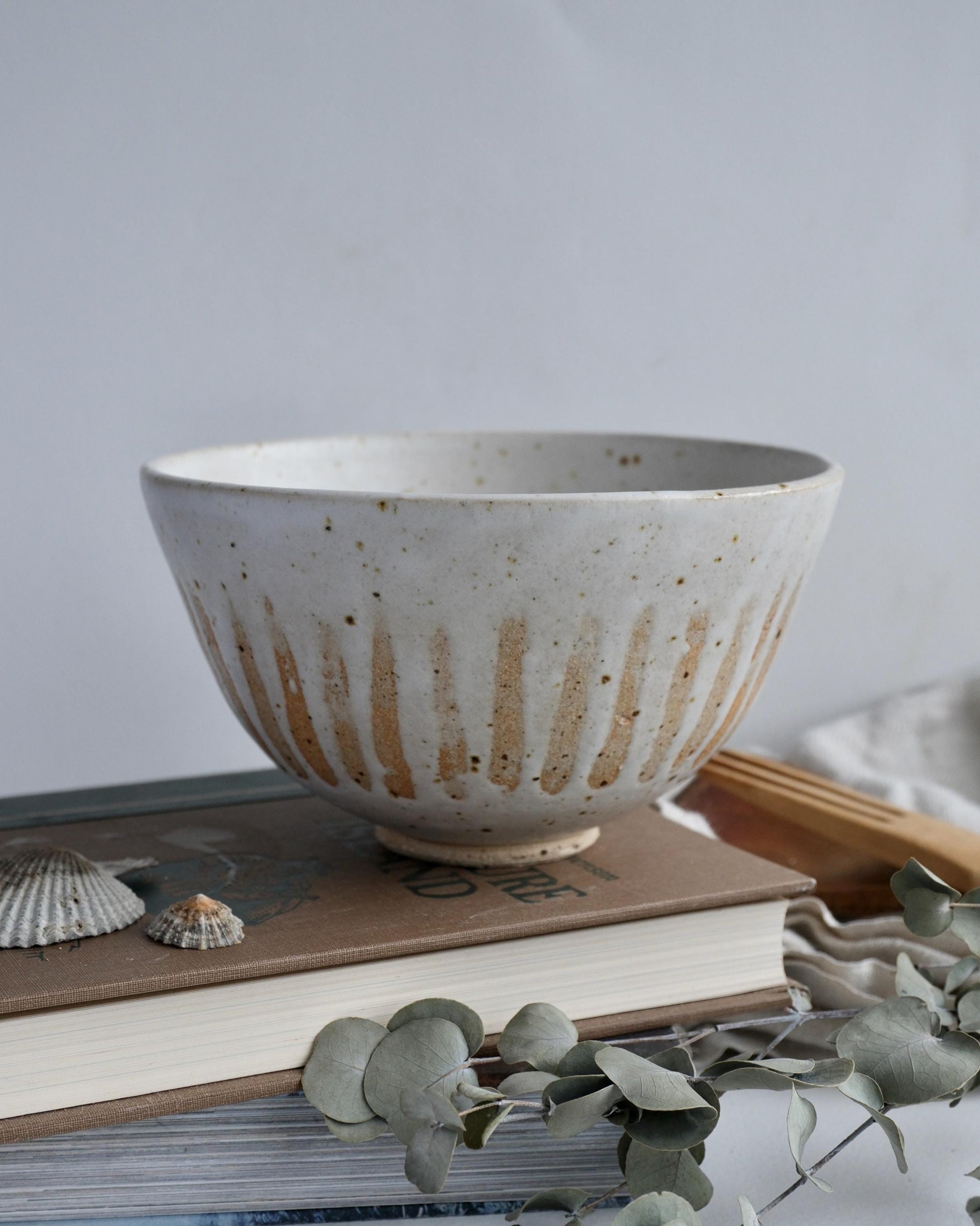 white Ceramic bowl with rustic striped design on top of books with a light background