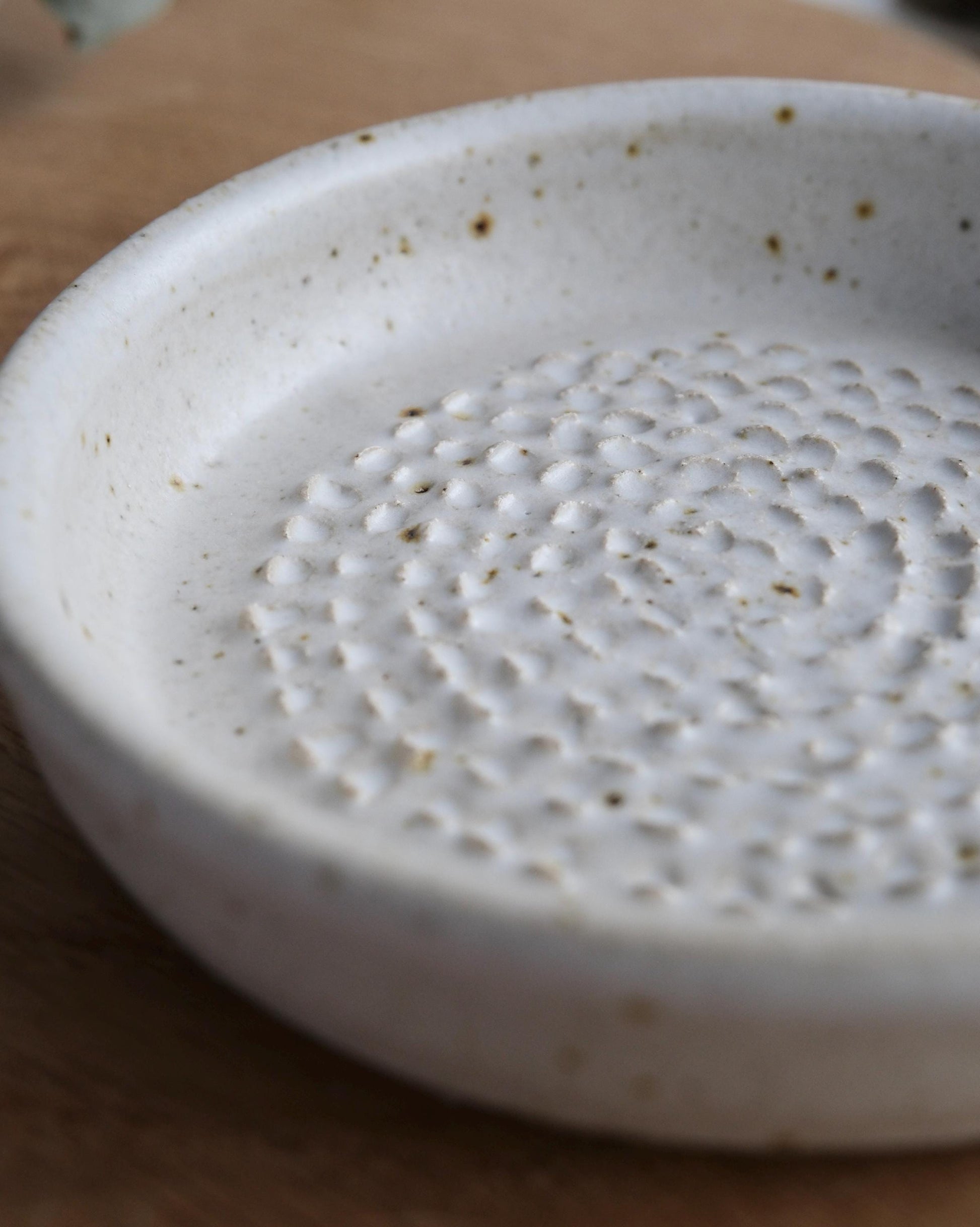 Close-up of a textured white ceramic grater dish on a wooden surface