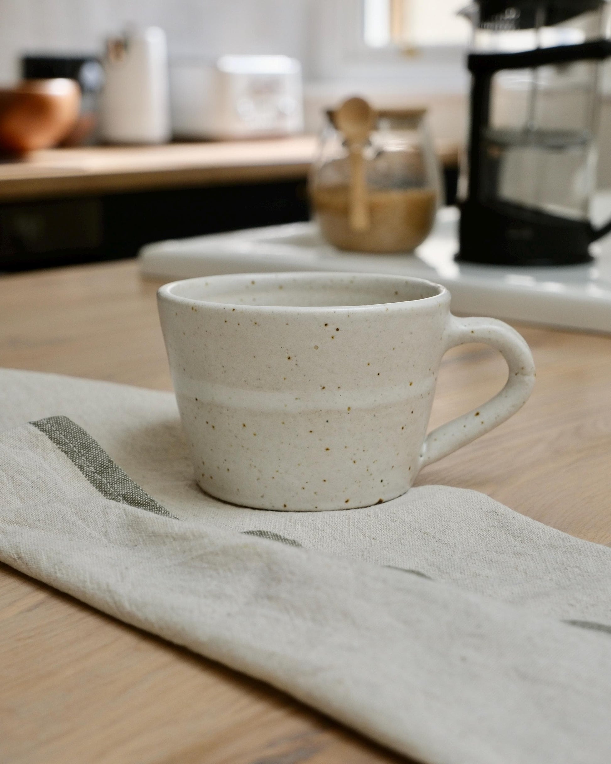 white Speckled ceramic coffee mug on a kitchen counter with a blurred background