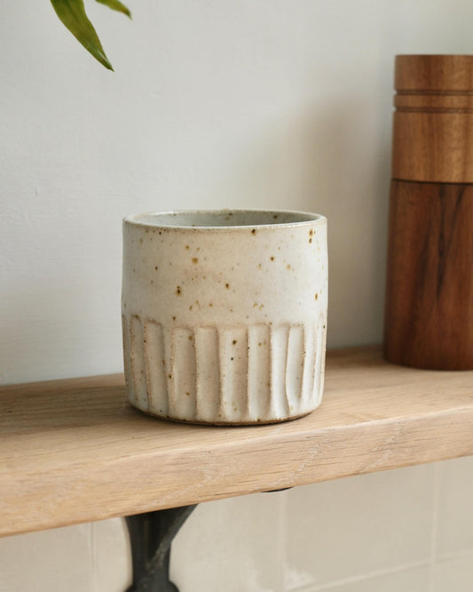 white Ceramic flat white cup with textured line design on a wooden shelf