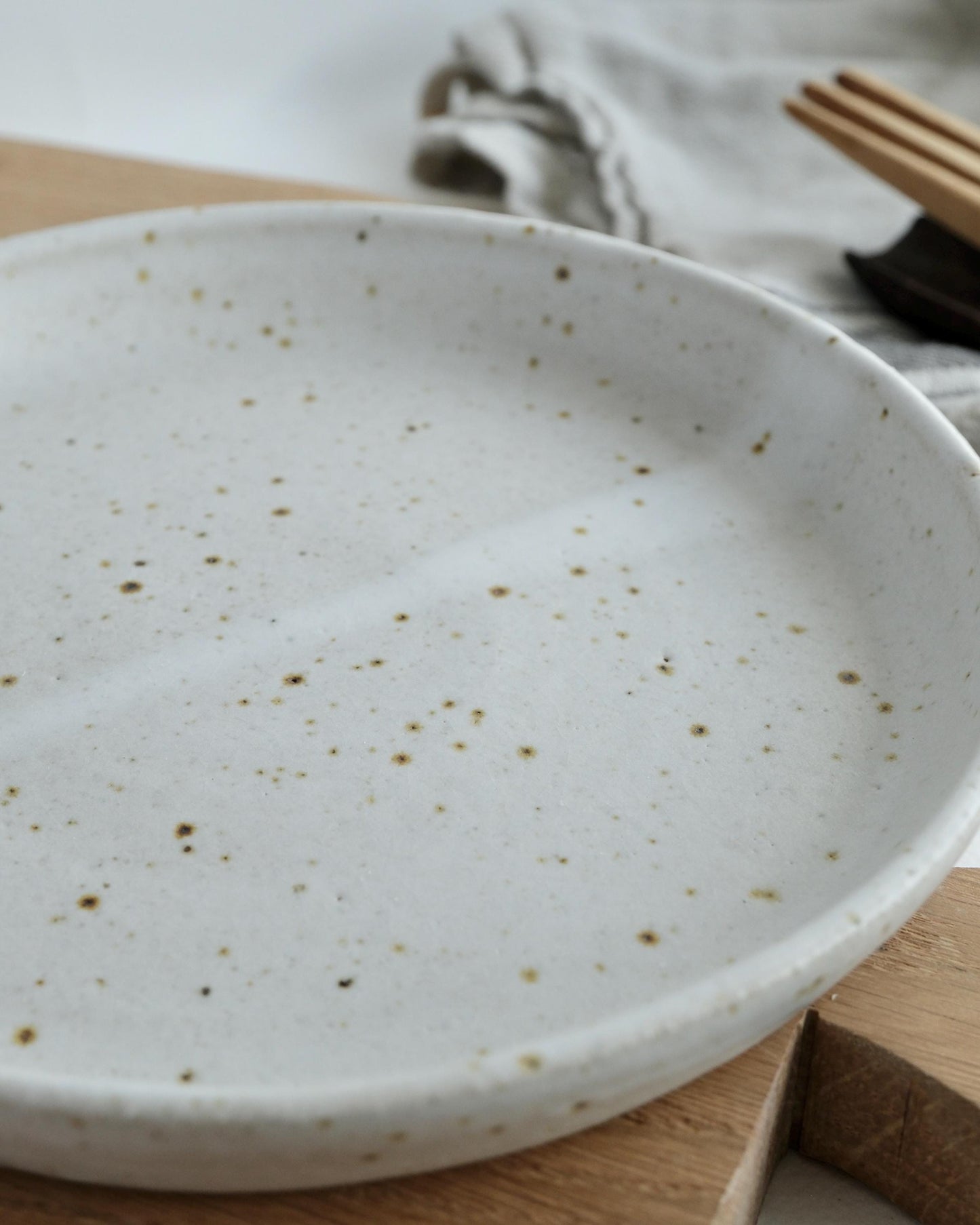 Speckled ceramic small side plate on a wooden surface with a cloth and fork in the background