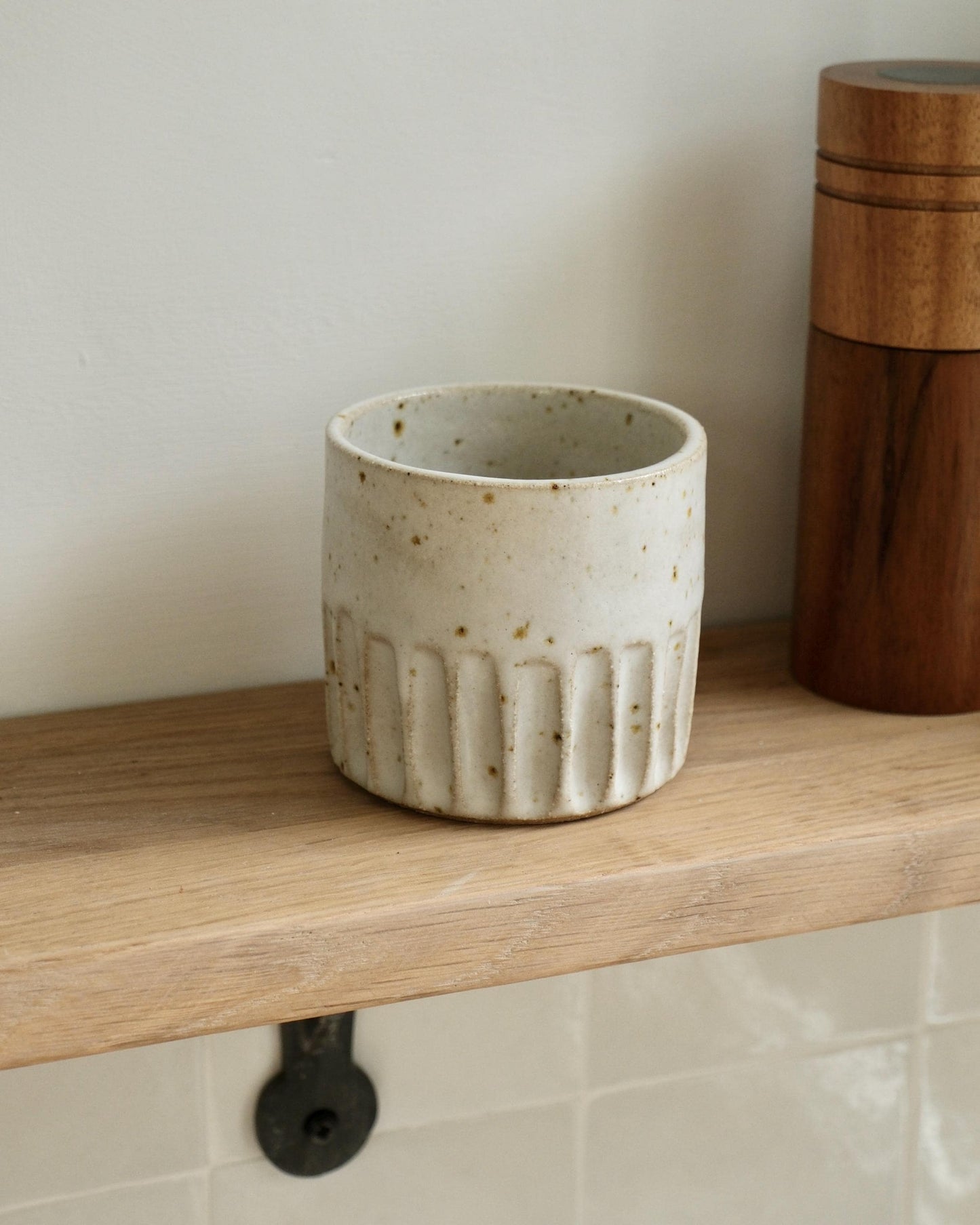 Ceramic pot with textured line design on a wooden shelf against a neutral wall.