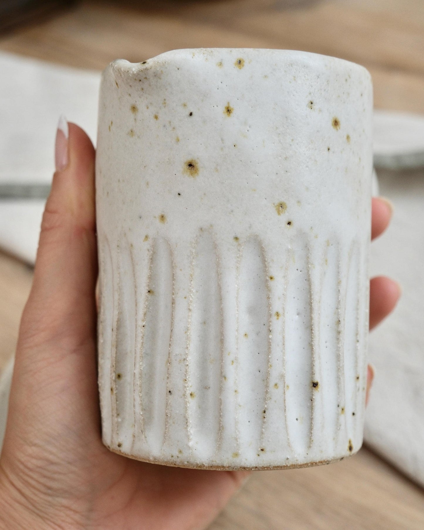 Hand holding a textured ceramic milk jug with a line surface texture and a blurred background