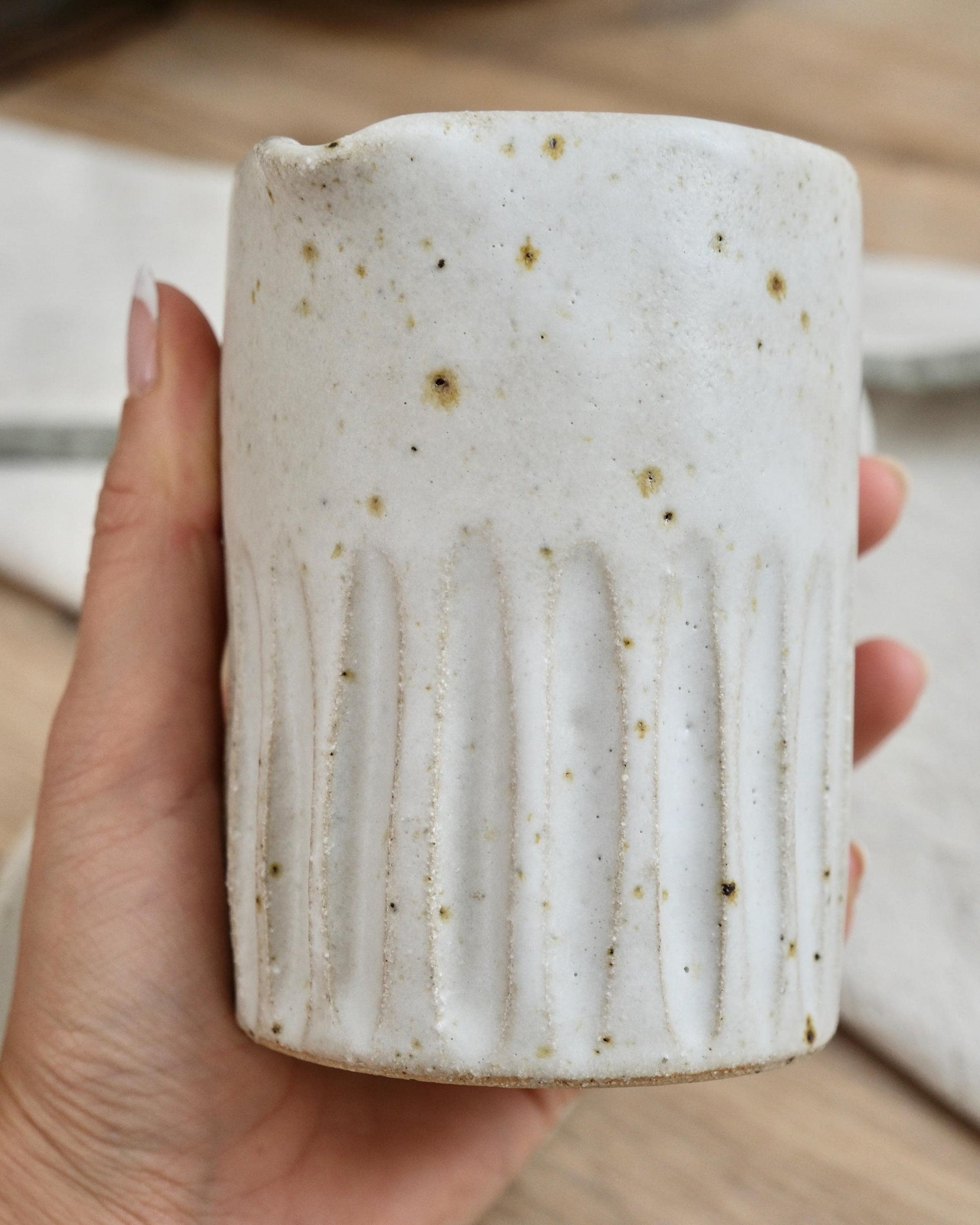 Hand holding a textured ceramic milk jug with a line surface texture and a blurred background