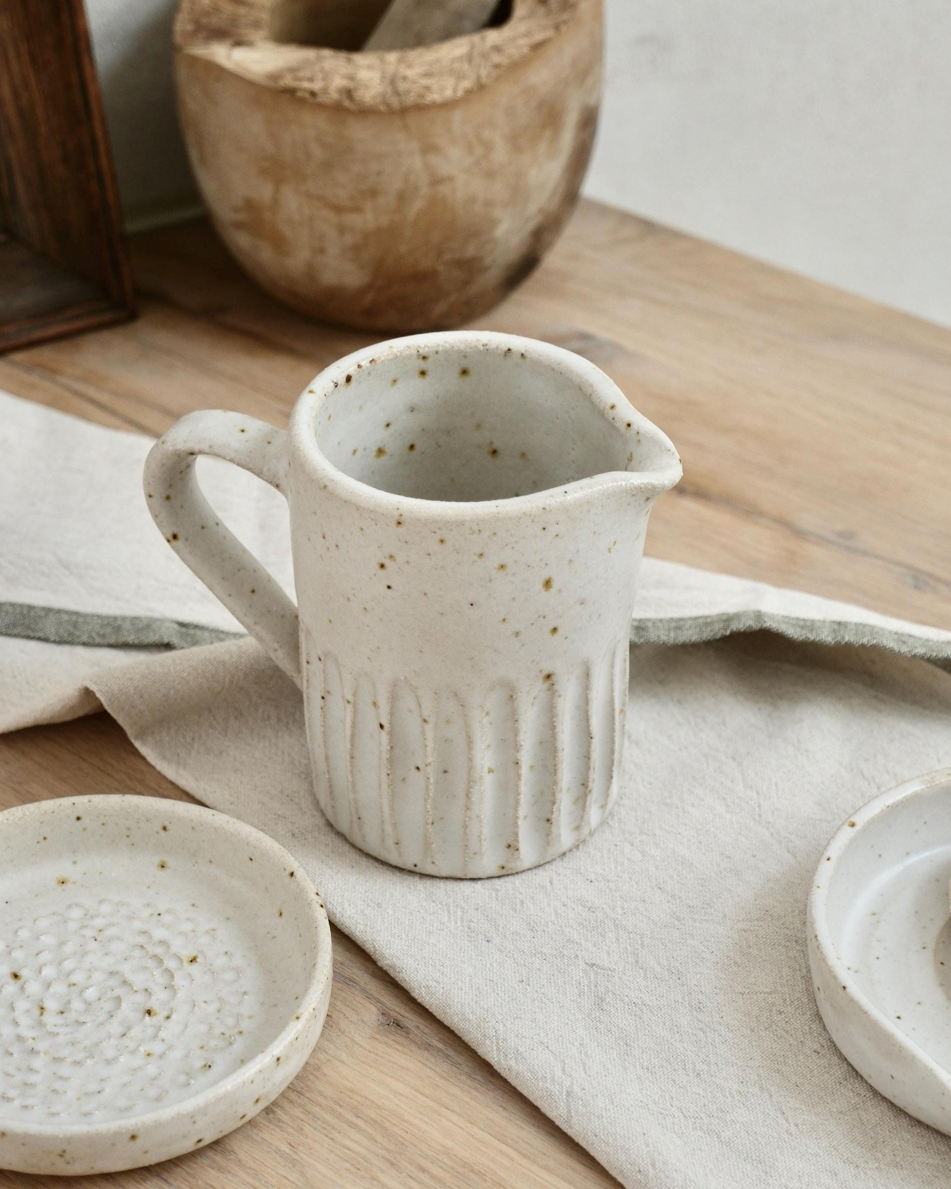 white speckled Ceramic pitcher with textured line surface on a wooden table with a cloth