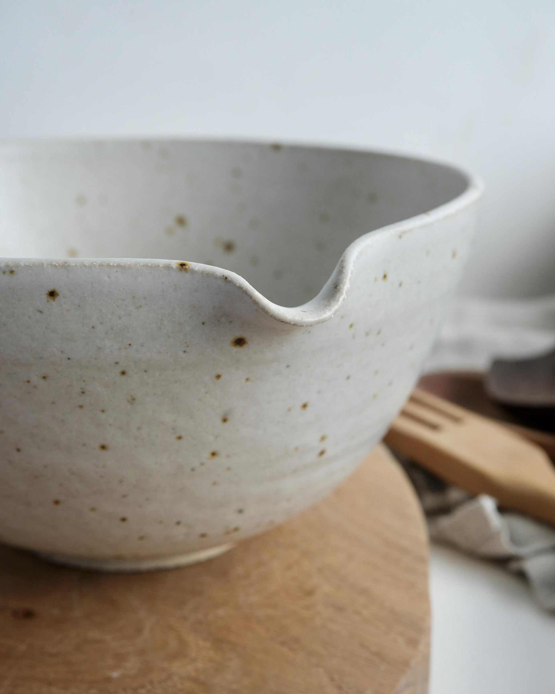 white Speckled ceramic mixing bowl with a pouring spout on a wooden surface with a blurred background
