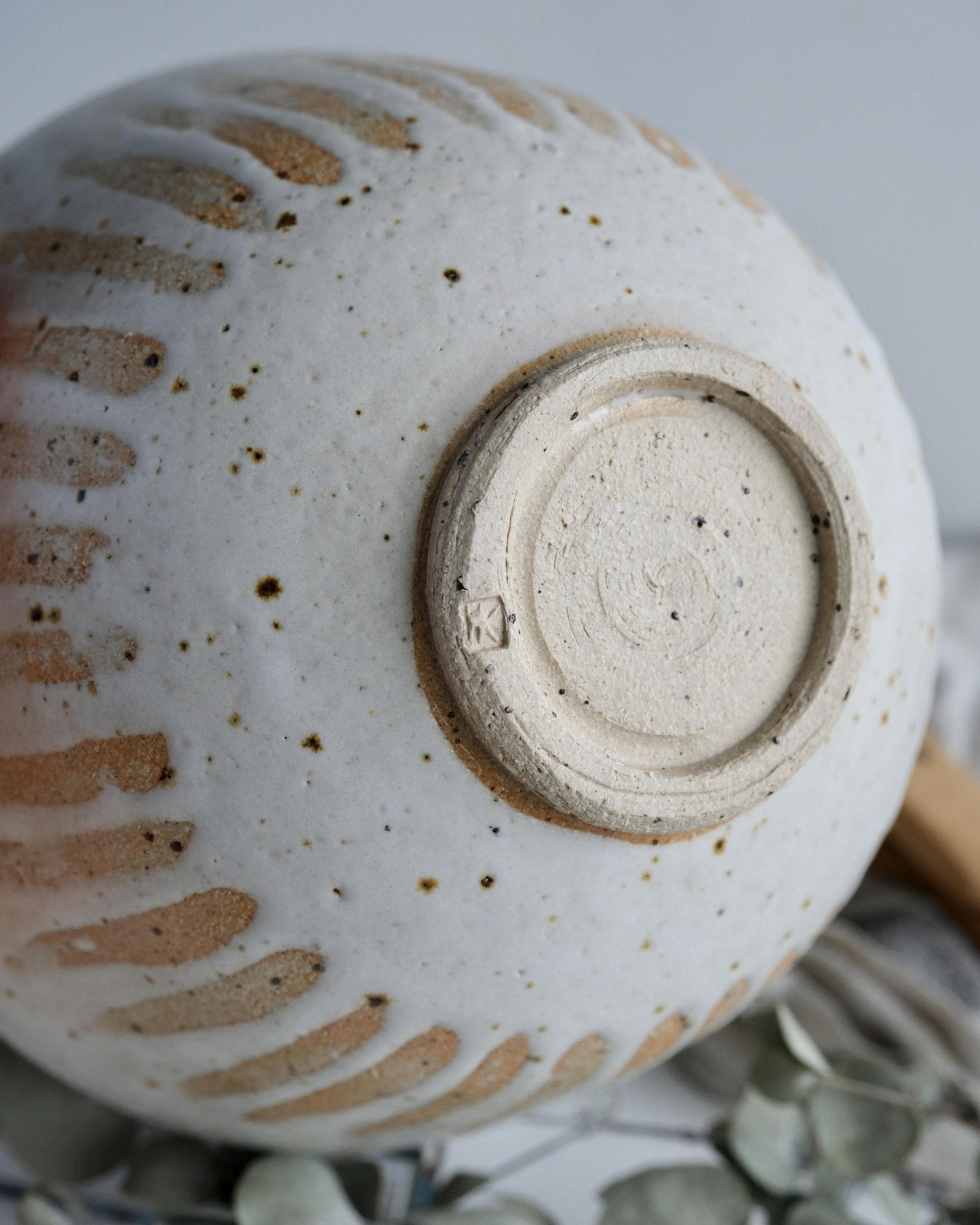 Close-up of a the bottom of a white ceramic bowl with textured surface and visible makers mark.