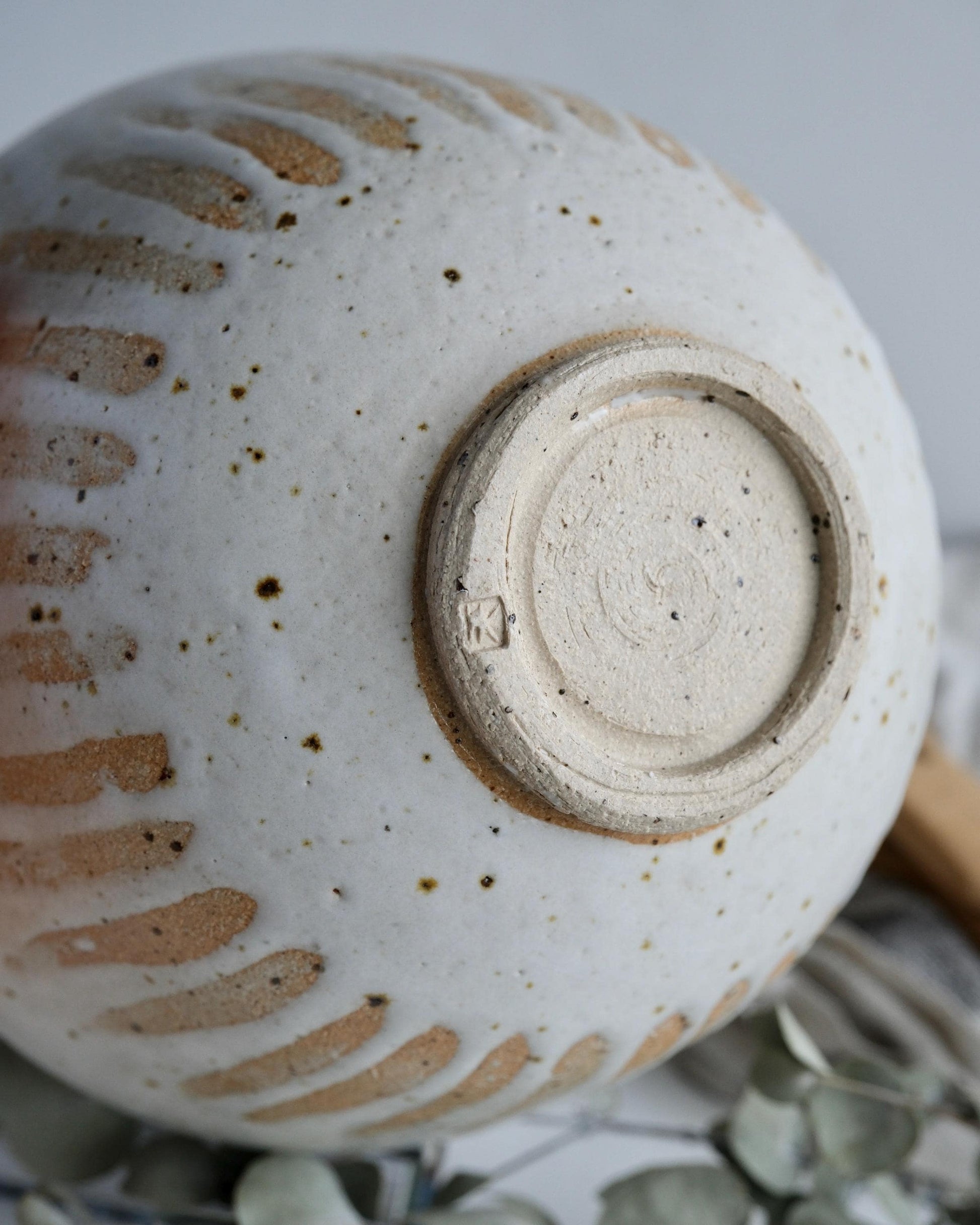 Close-up of a the bottom of a white ceramic bowl with textured surface and visible makers mark.