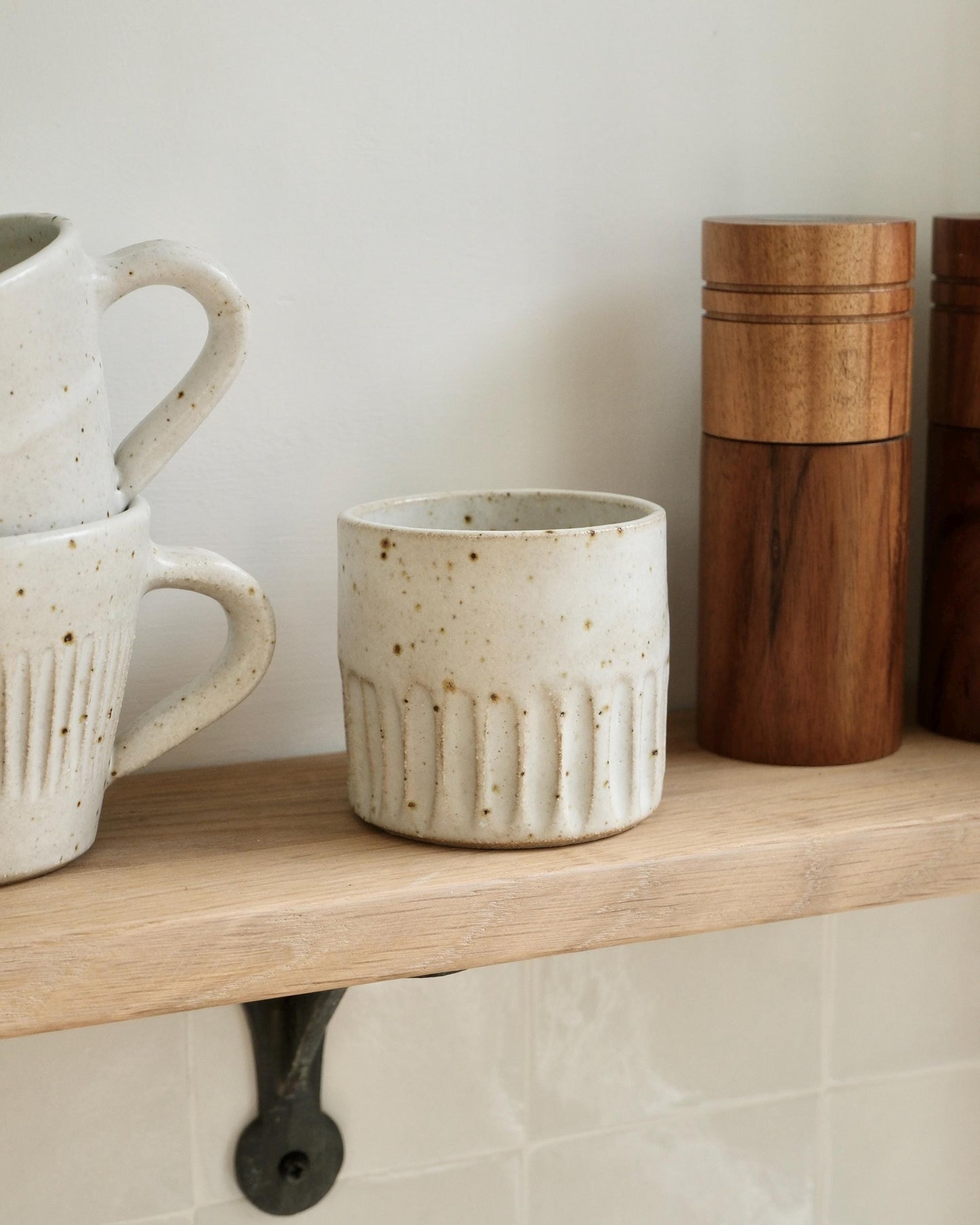 white Ceramic mugs and a wooden container on a shelf against a white wall.