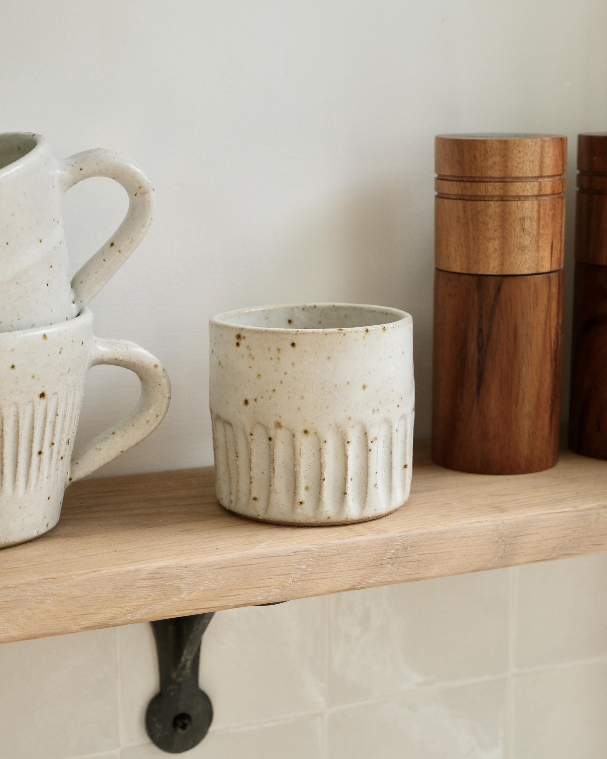 white Ceramic mugs and a wooden container on a shelf against a white wall.