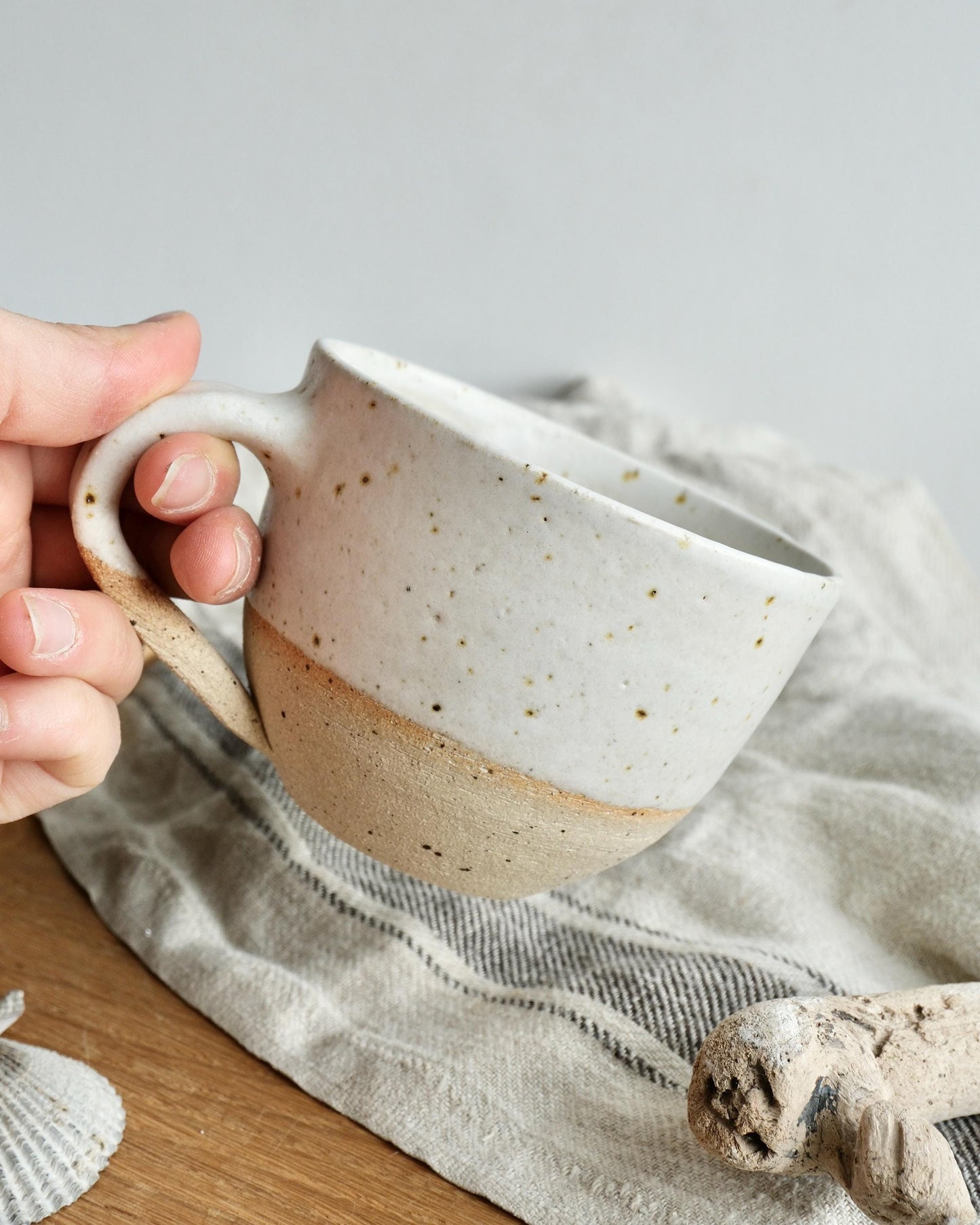 Hand holding a white ceramic mug with speckled design on a textured surface