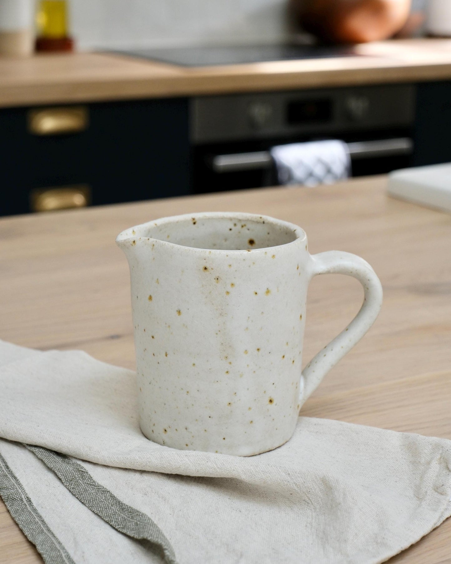 white Speckled ceramic pitcher milk jug on a kitchen counter with a blurred background