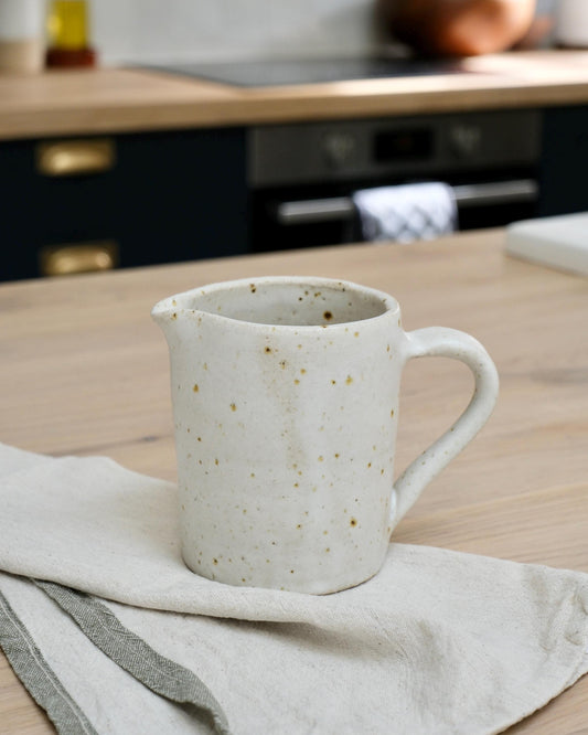 white Speckled ceramic pitcher milk jug on a kitchen counter with a blurred background