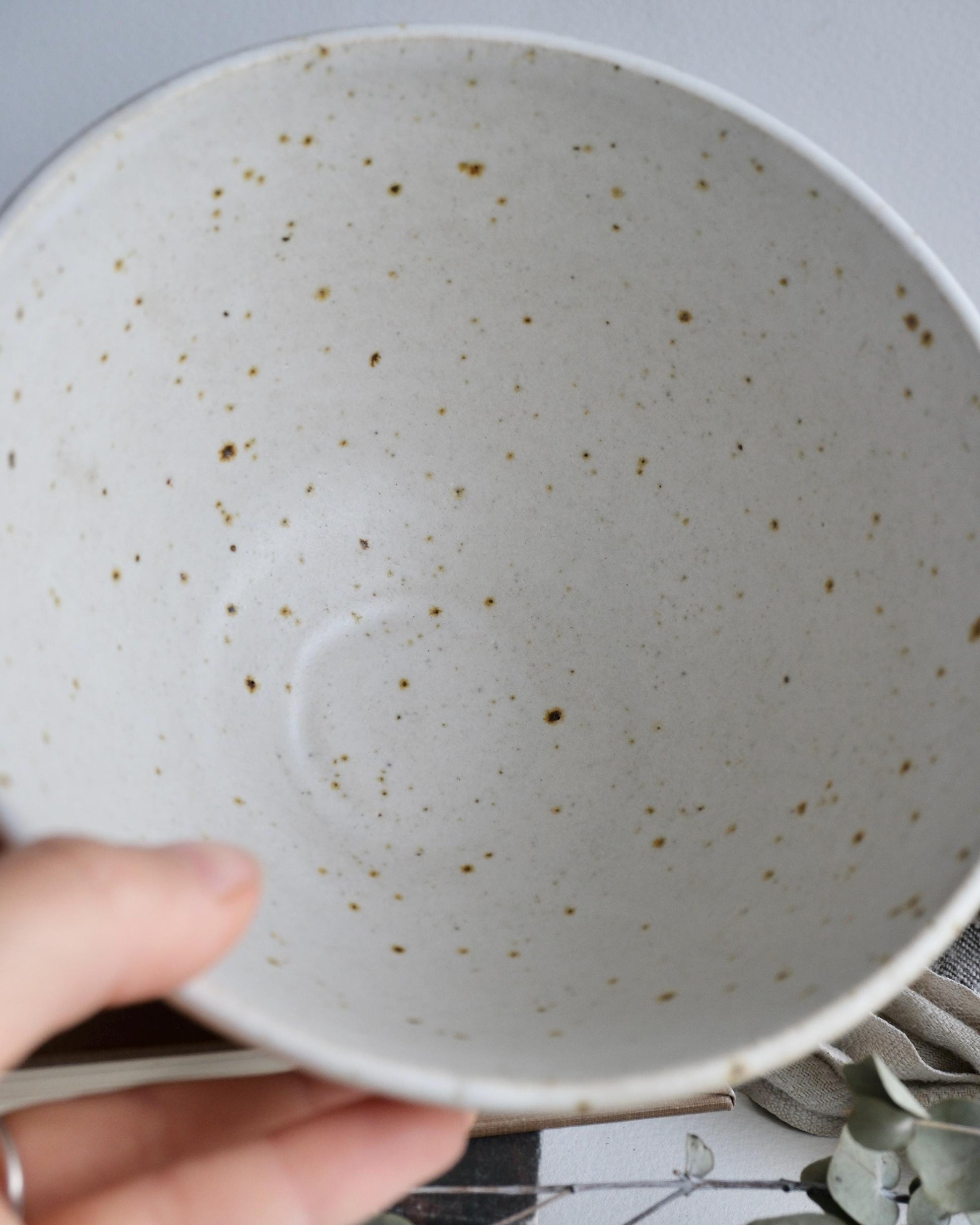 Close-up of a white speckled ceramic bowl held by a hand.