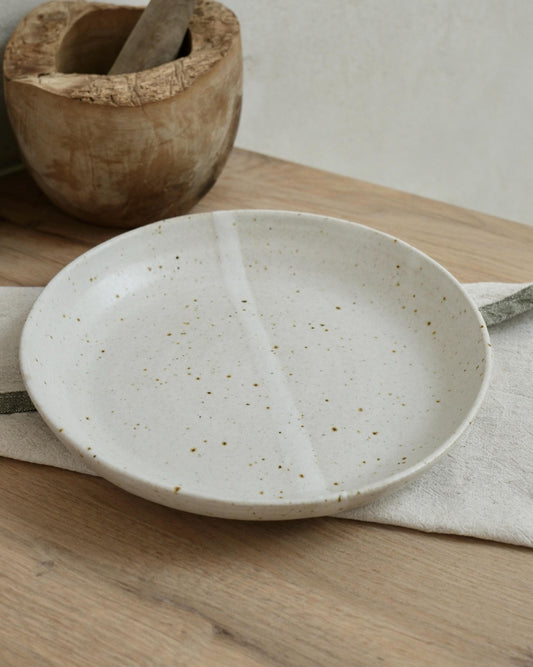 White Speckled ceramic pasta bowl on a wooden surface with a wooden bowl in the background