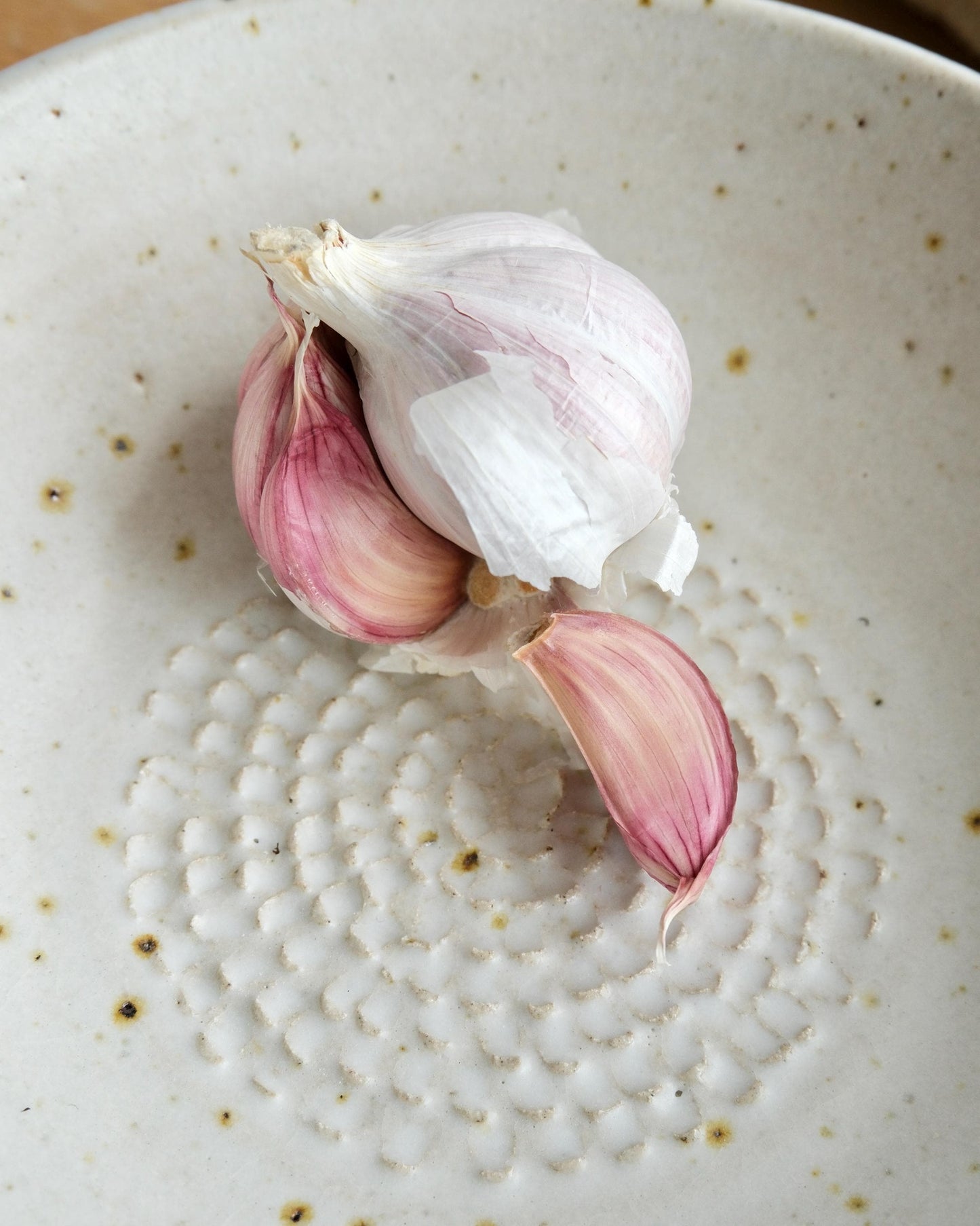 Garlic bulb with pink cloves on a textured ceramic plate
