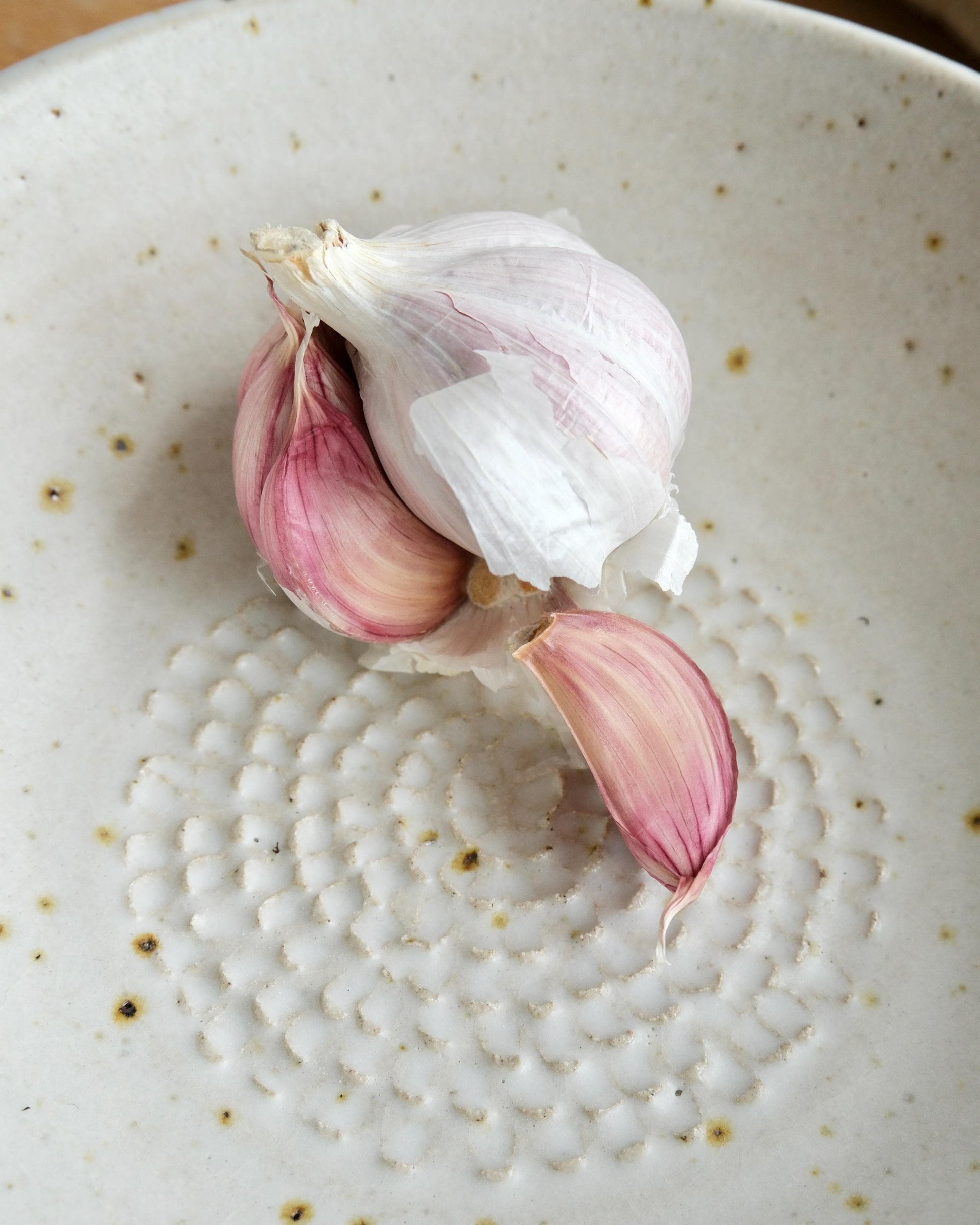 Garlic bulb with pink cloves on a textured ceramic plate