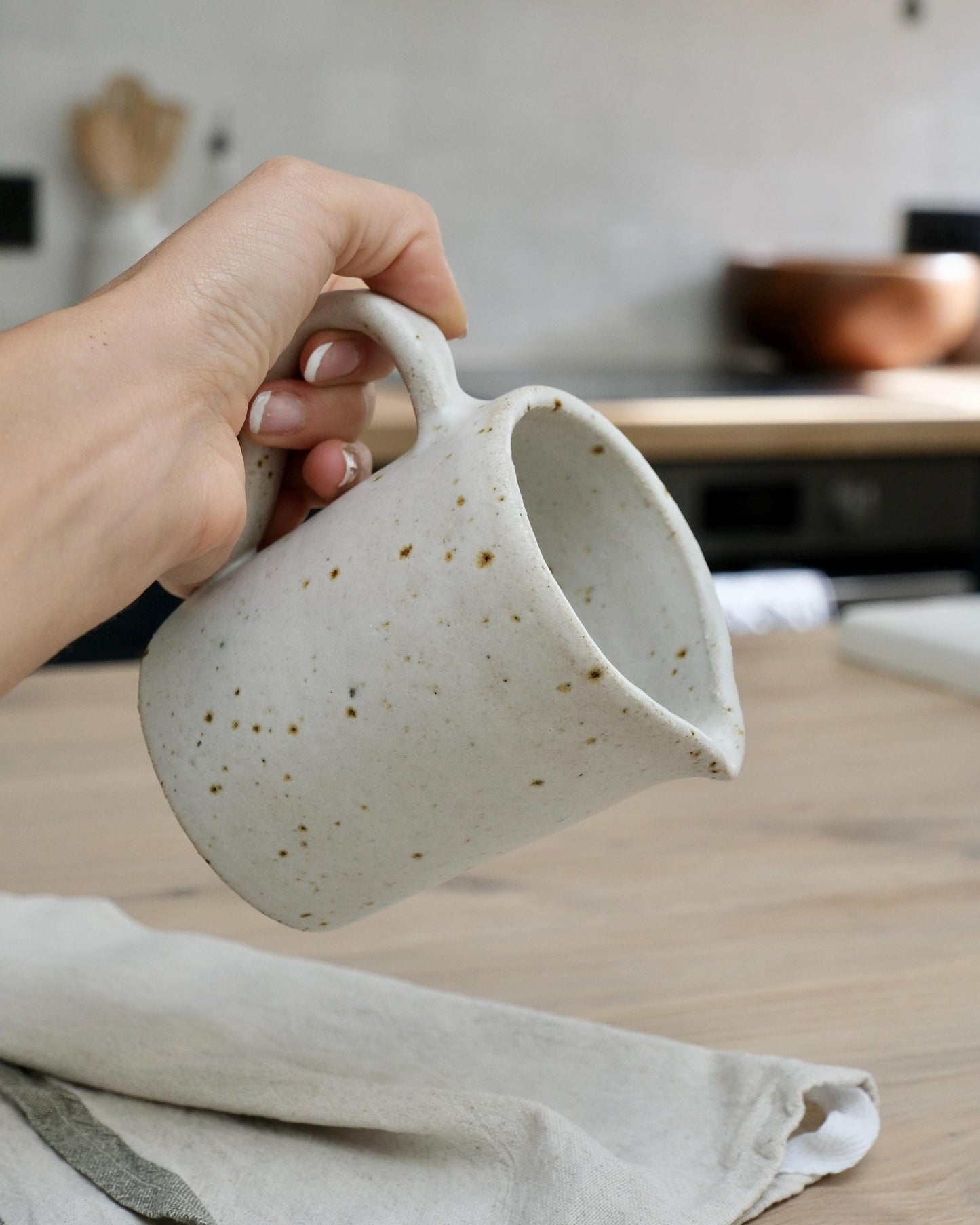 Hand holding a white speckled ceramic mug with speckled texture on a wooden surface.