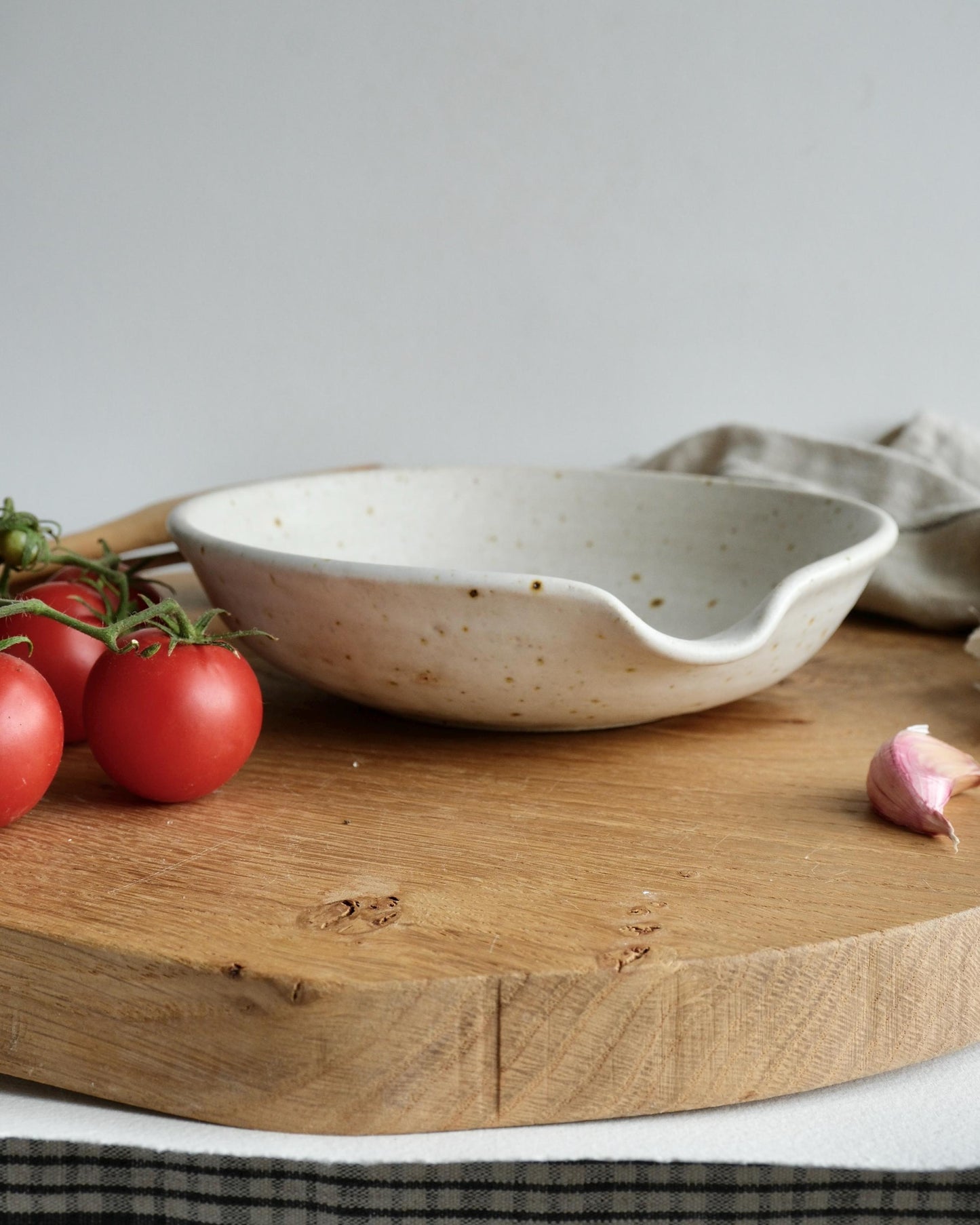 White ceramic grater bowl on a wooden cutting board with tomatoes and garlic.