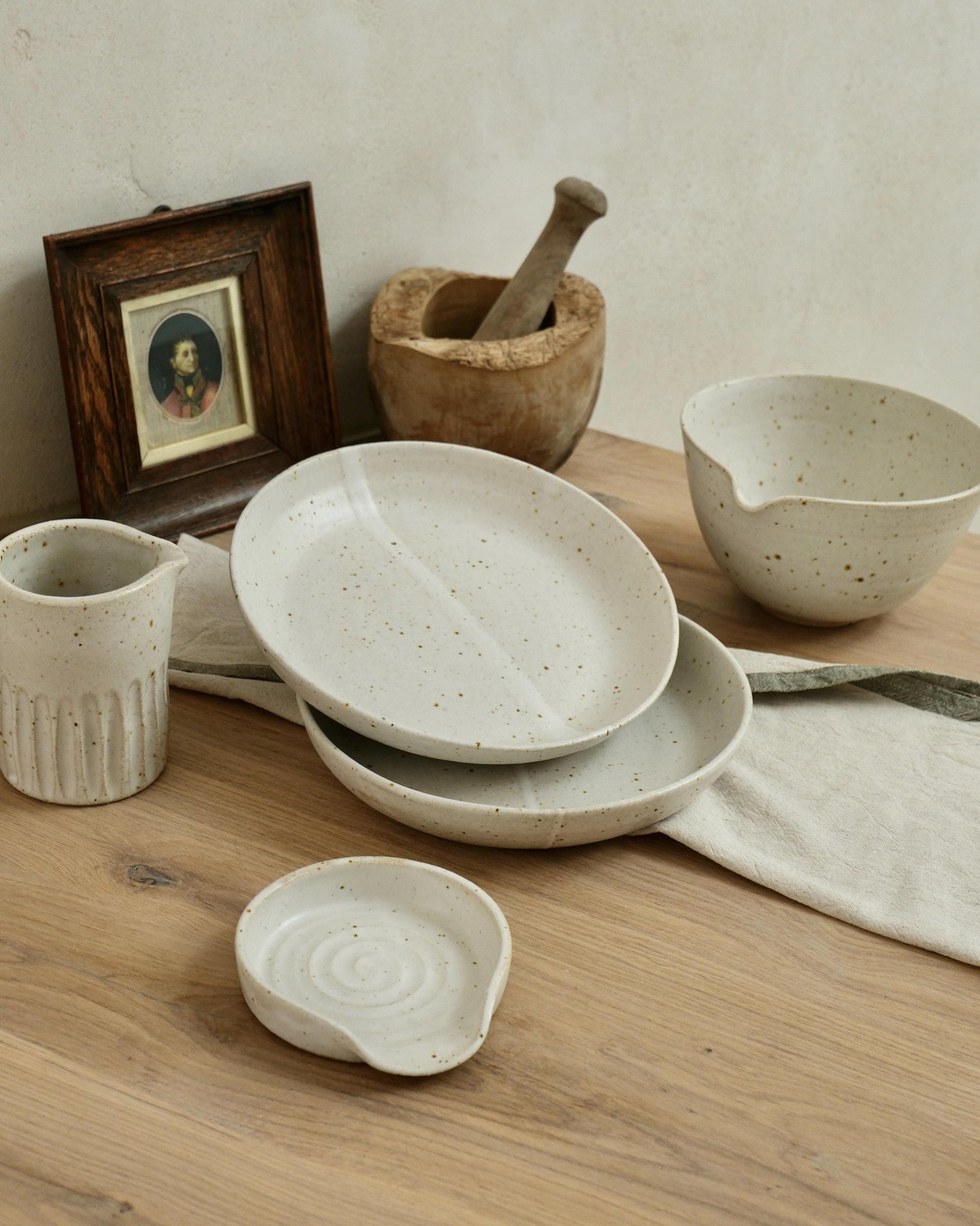 Set of handmade white speckled ceramic dishes on a wooden surface with a neutral background