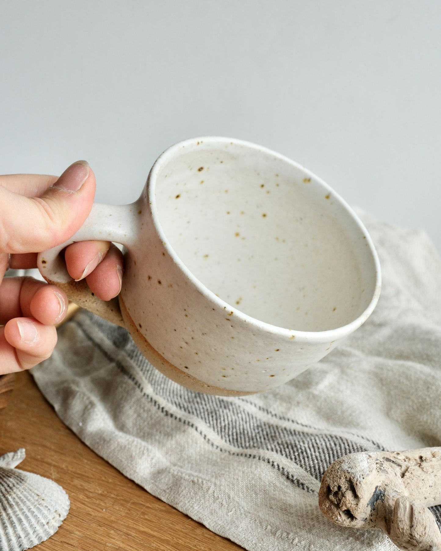 Hand holding a white ceramic mug with a speckled pattern on a light background