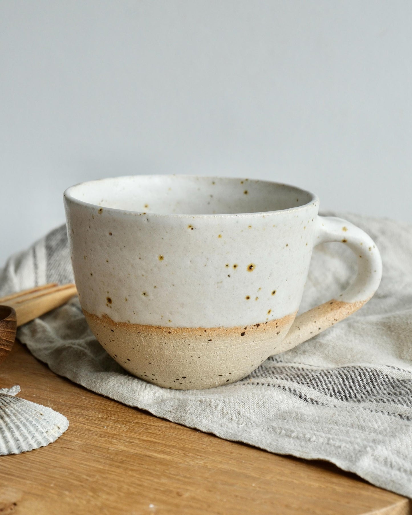 white Speckled ceramic coffee mug on a wooden surface with a light grey background