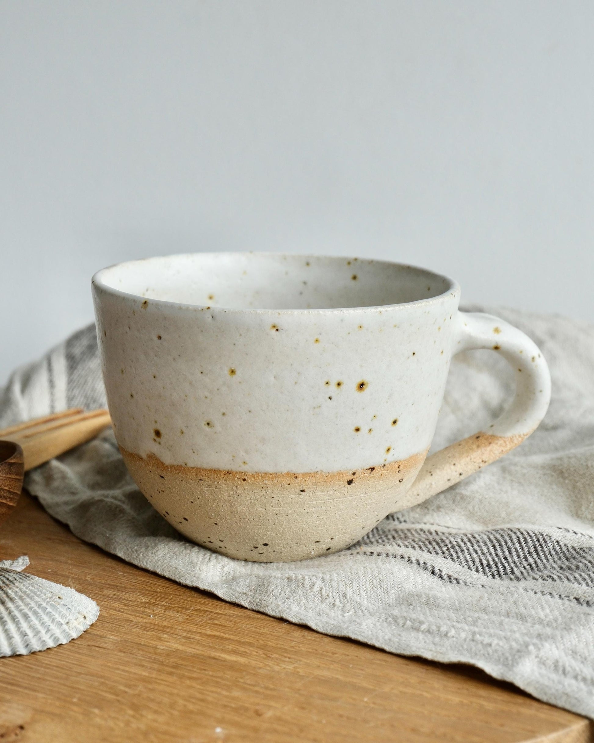 white Speckled ceramic coffee mug on a wooden surface with a light grey background