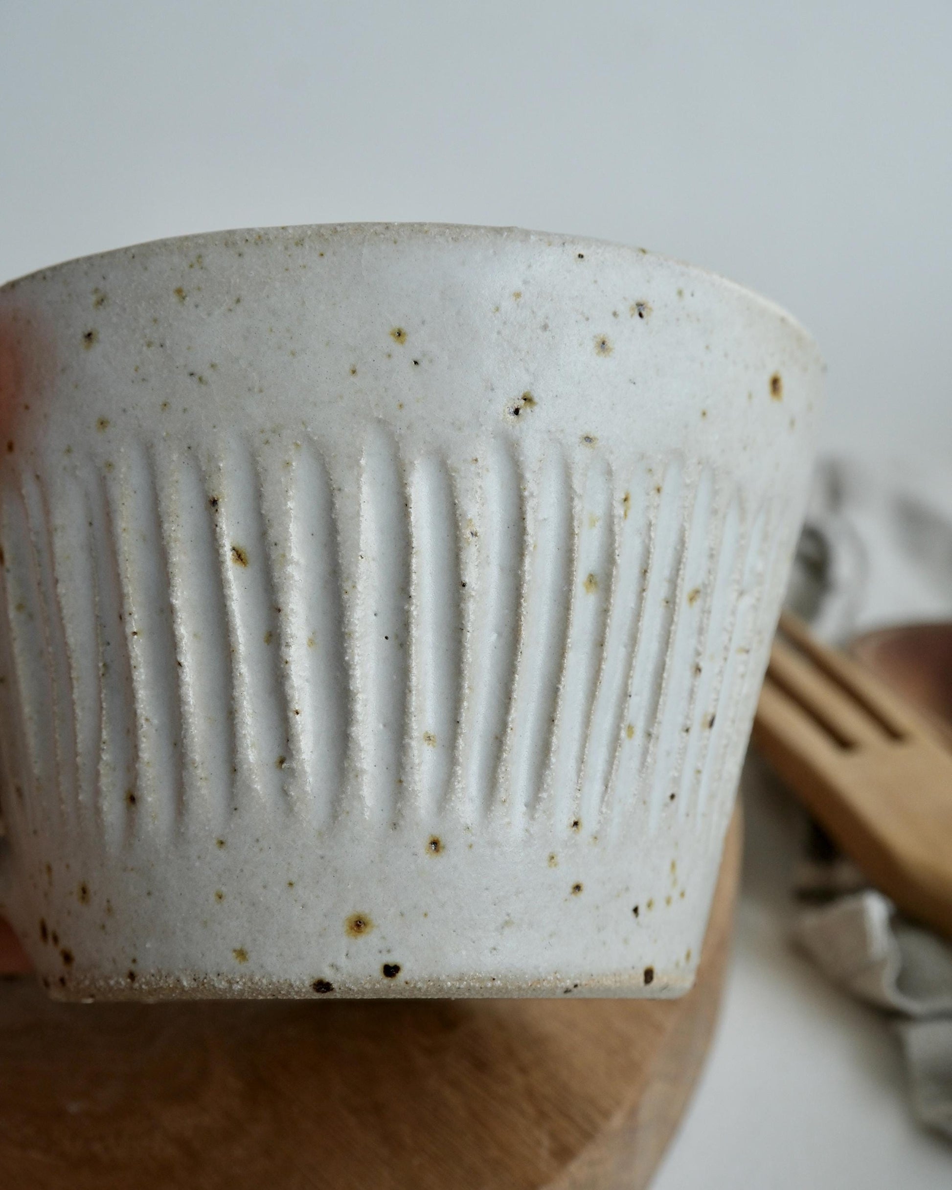 White speckled ceramic cup with textured line design on a wooden surface