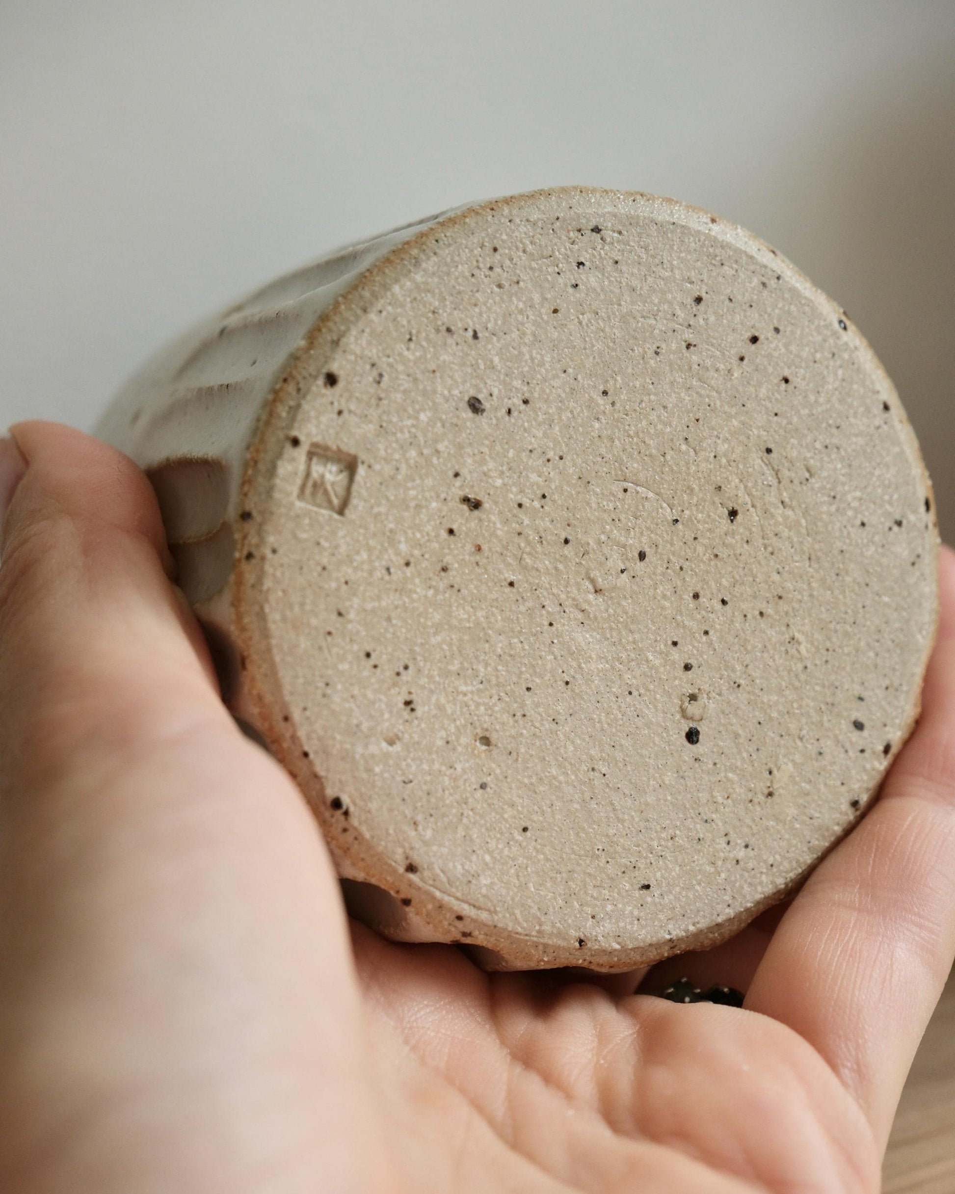 Hand holding a textured ceramic cup with a visible brand logo.