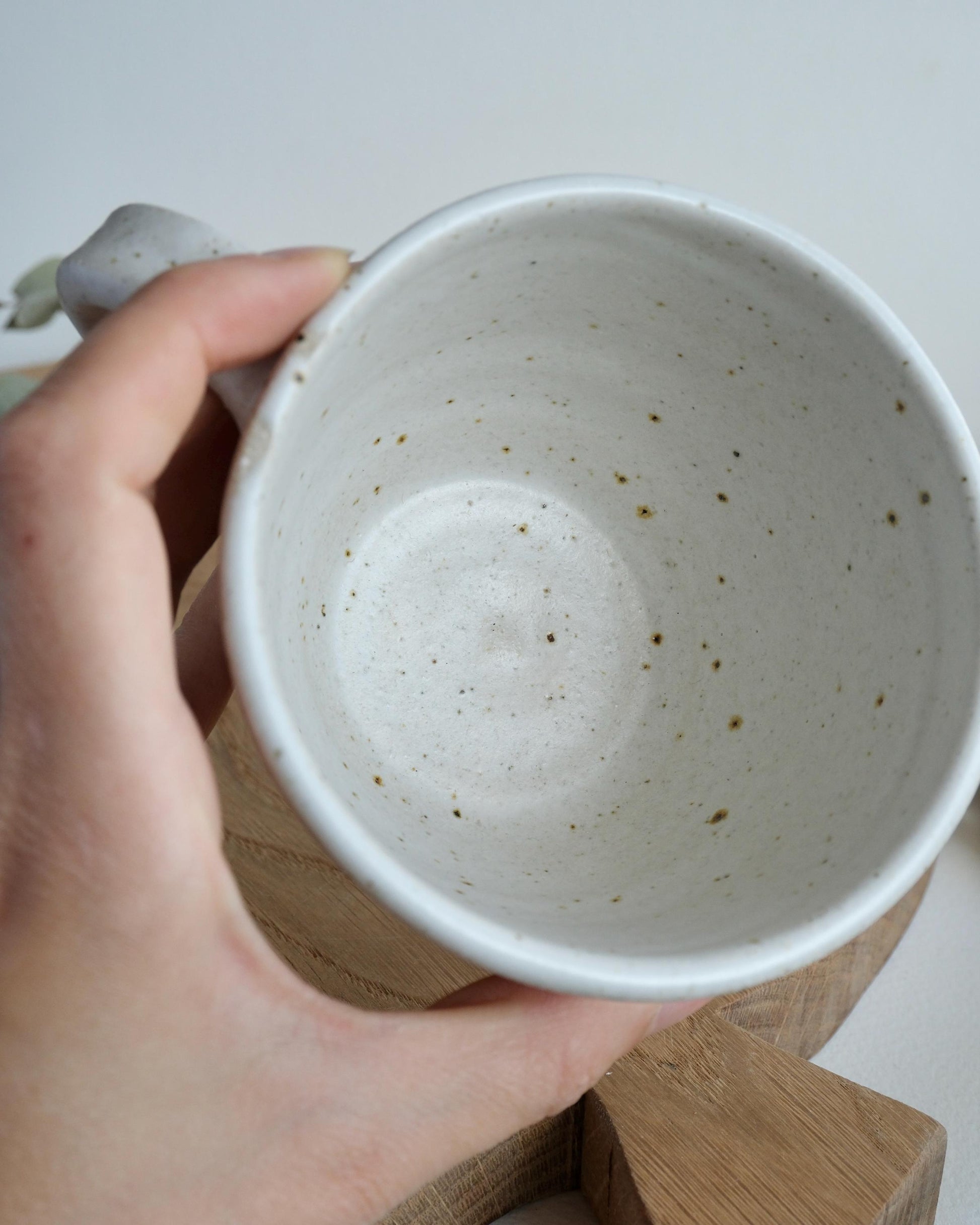 Hand holding a white speckled ceramic mug with a speckled pattern on a light background