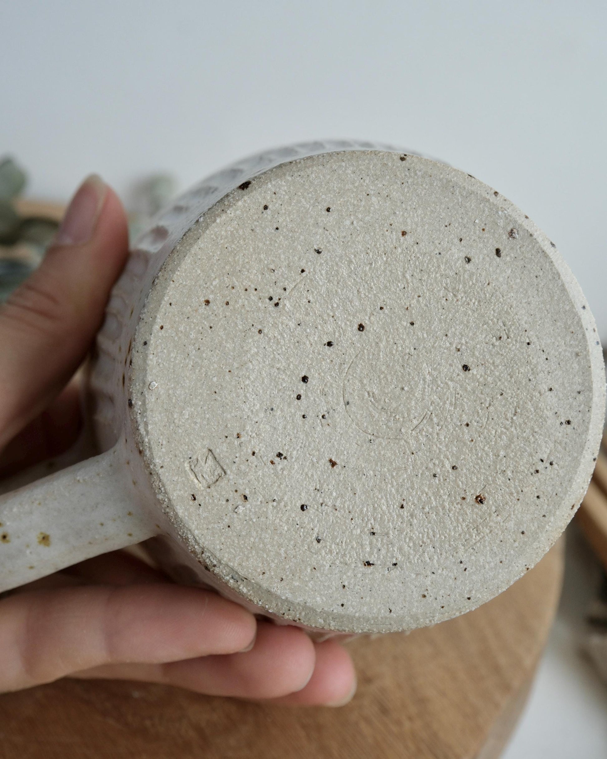 Close-up of a textured ceramic mug held by a hand on a light background