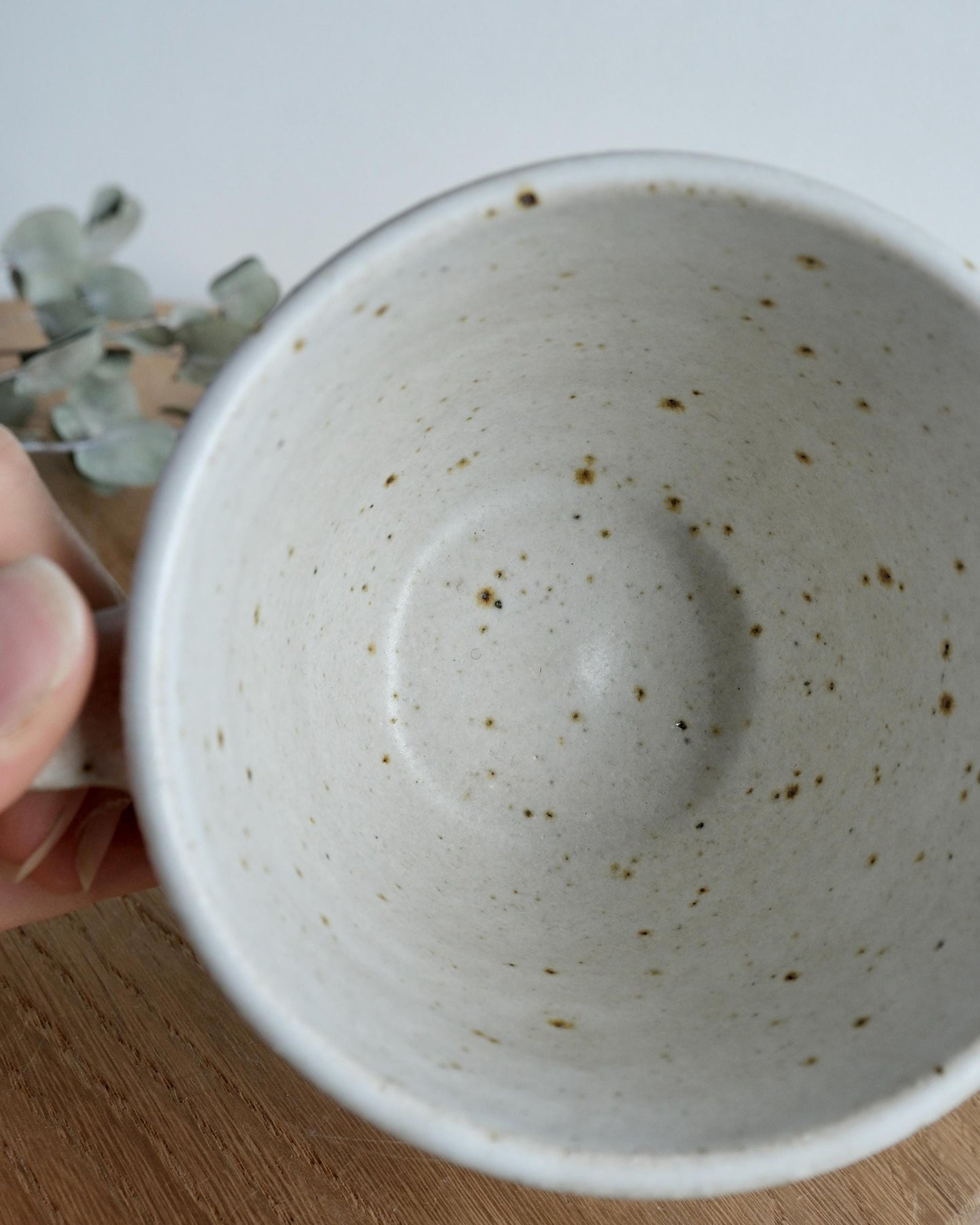 Speckled ceramic mug held by a hand on a wooden surface