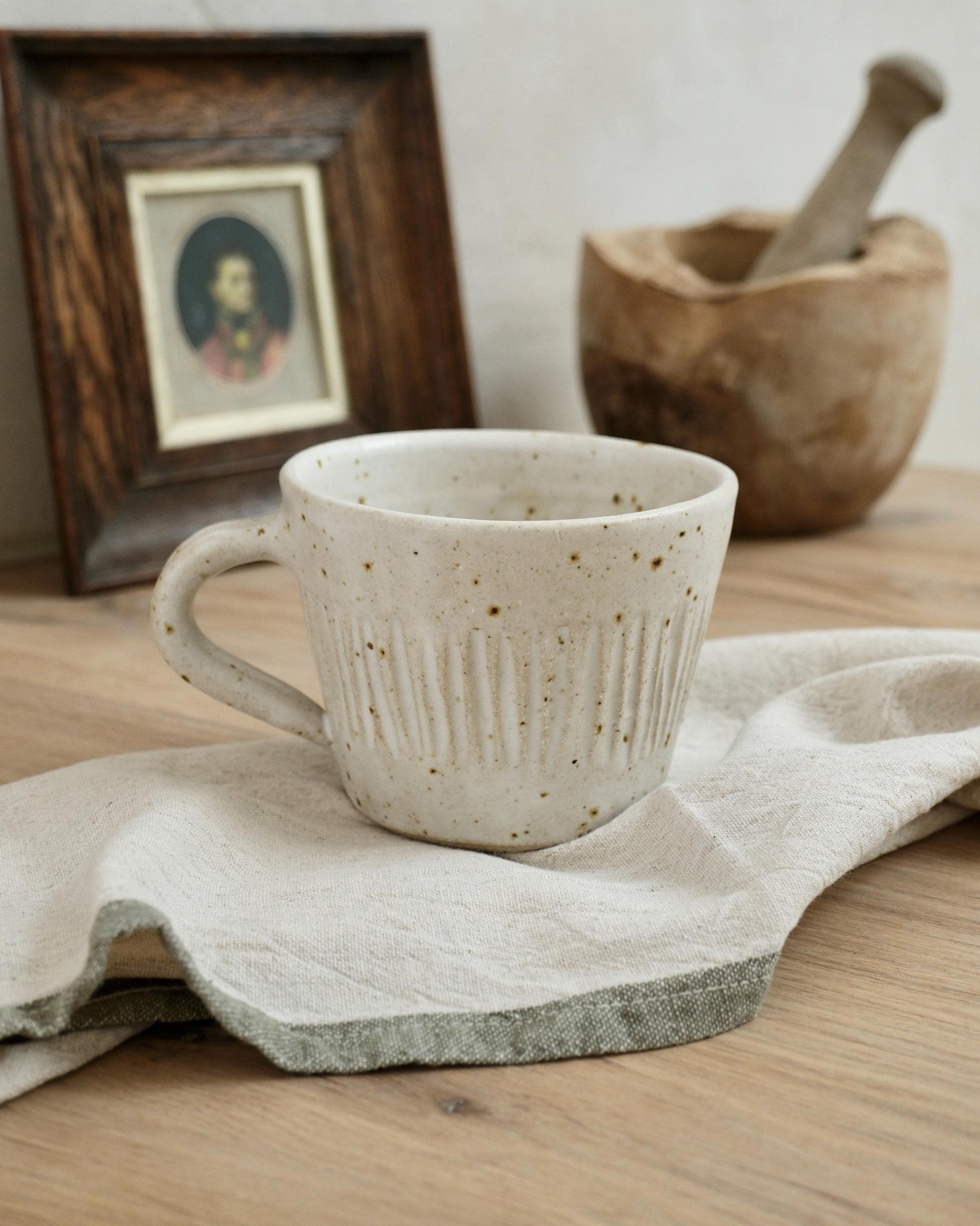White Ceramic mug with a line textured surface with a wooden frame and mortar and pestle in the background.