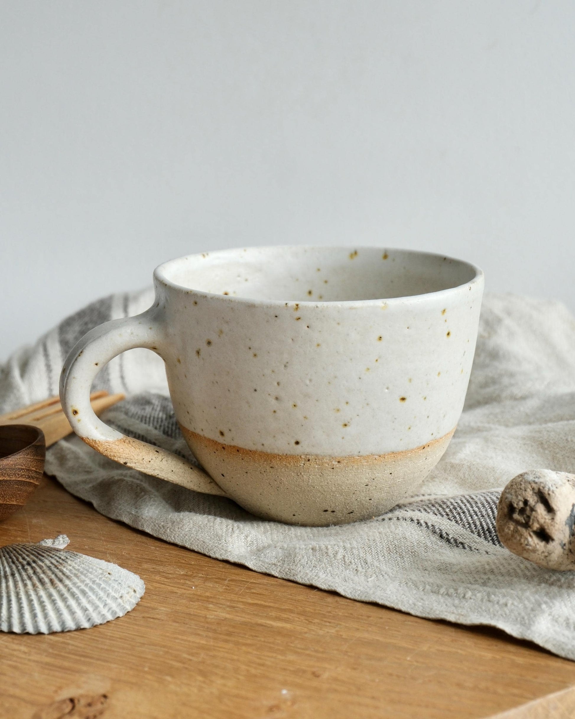handmade white Speckled ceramic mug on a wooden surface with a light grey background