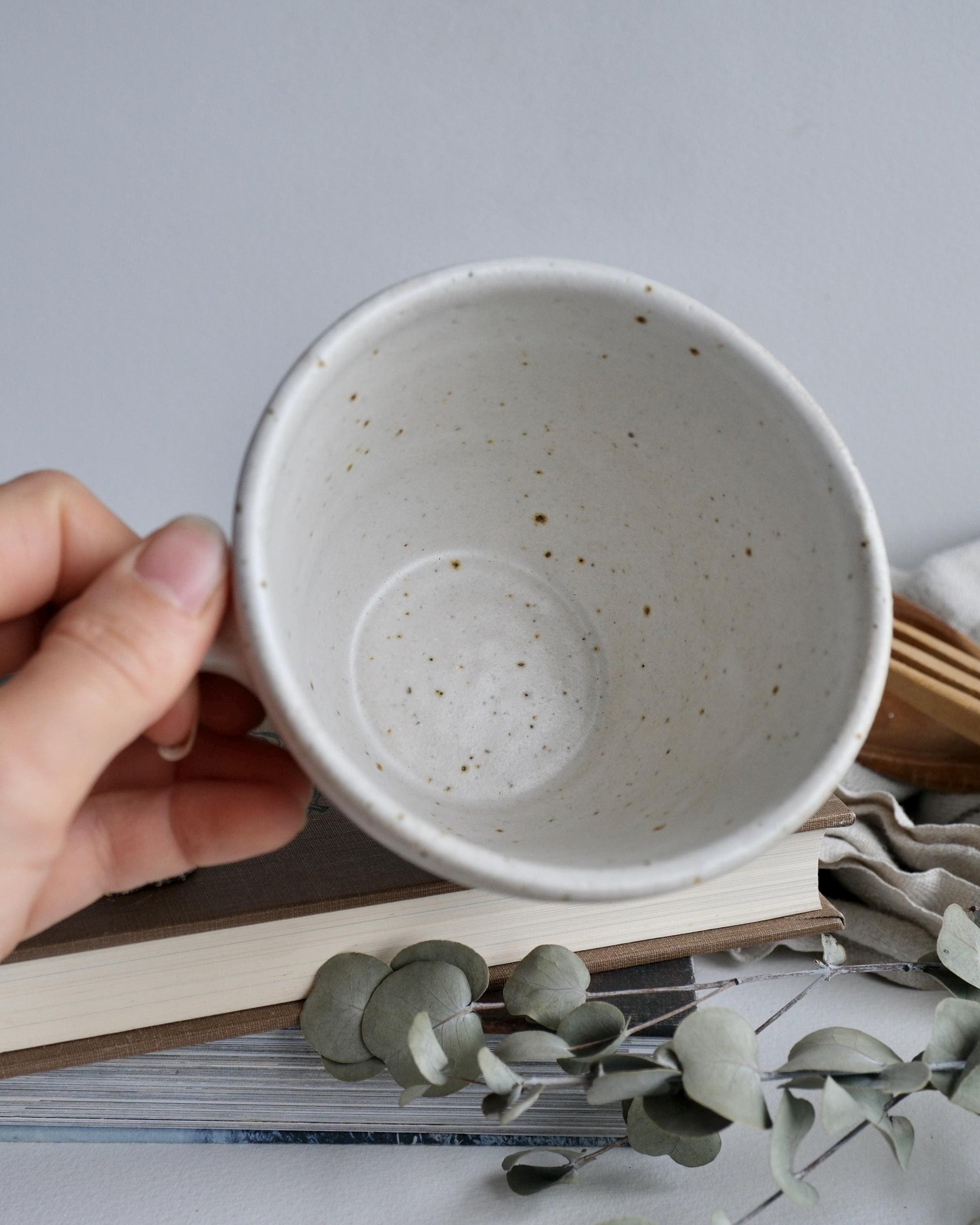 Hand holding a speckled ceramic cup with a minimal background