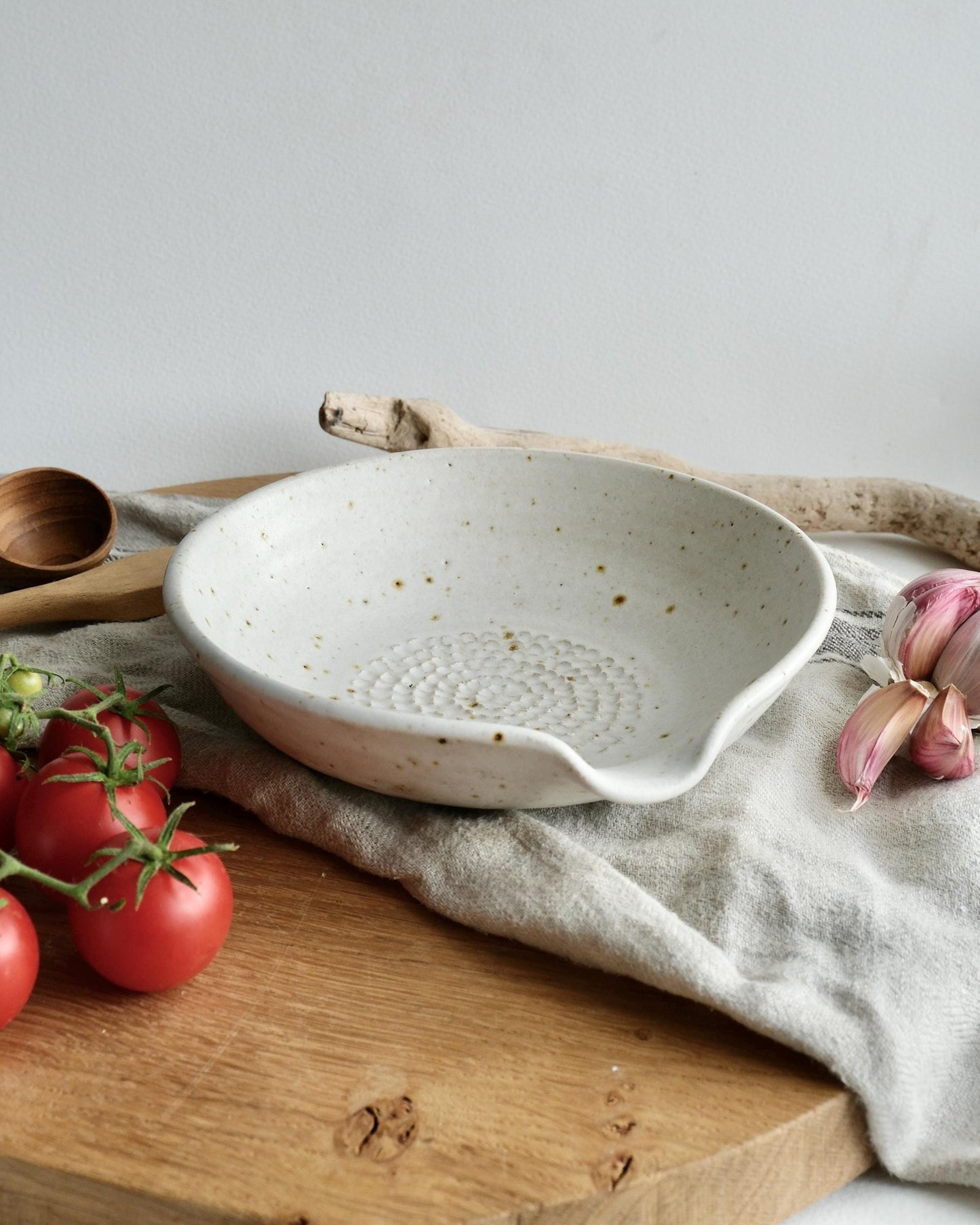 White ceramic grater dish on a wooden surface with tomatoes and garlic