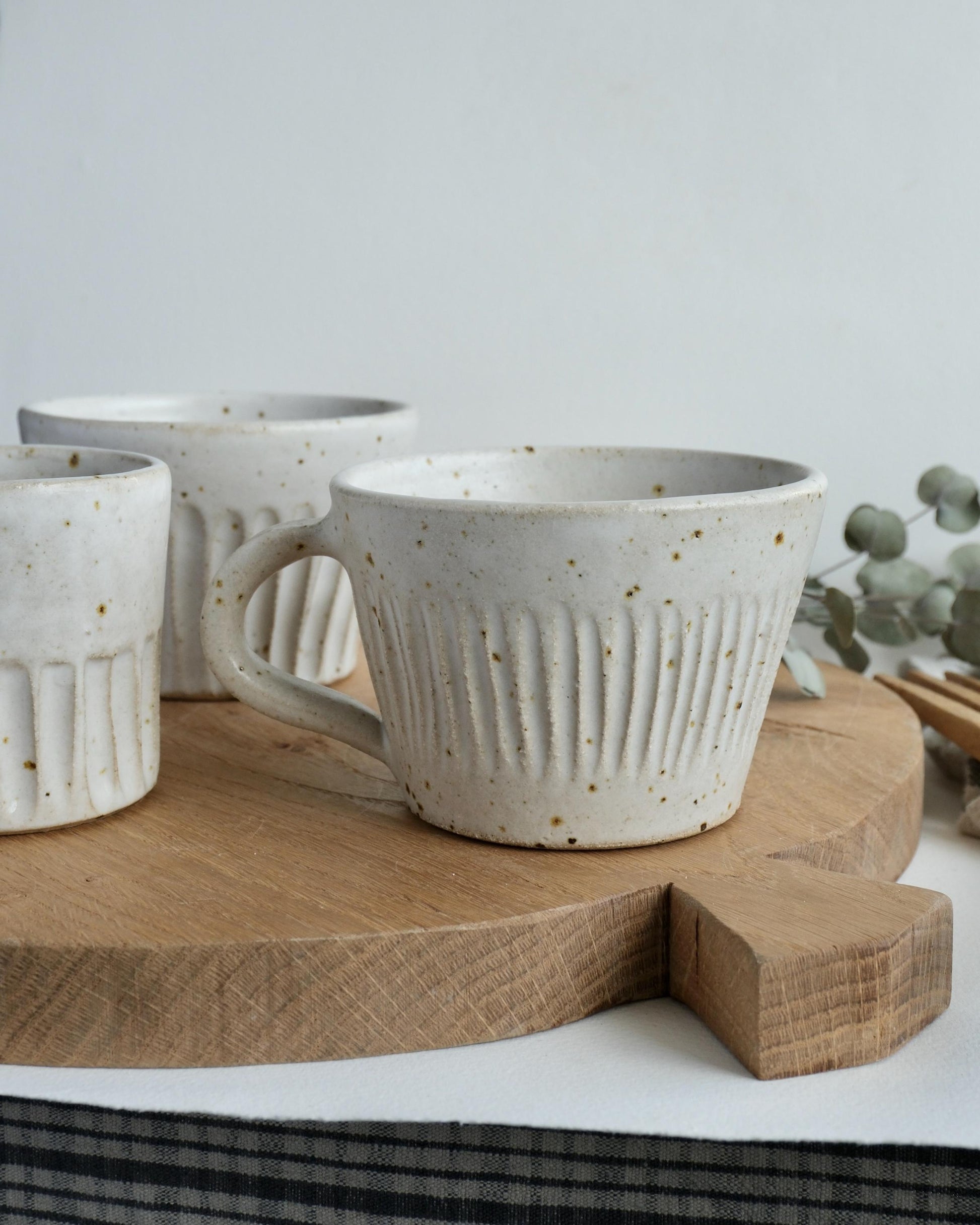 Three ceramic mugs with line pattern textured surfaces on a wooden board against a light background