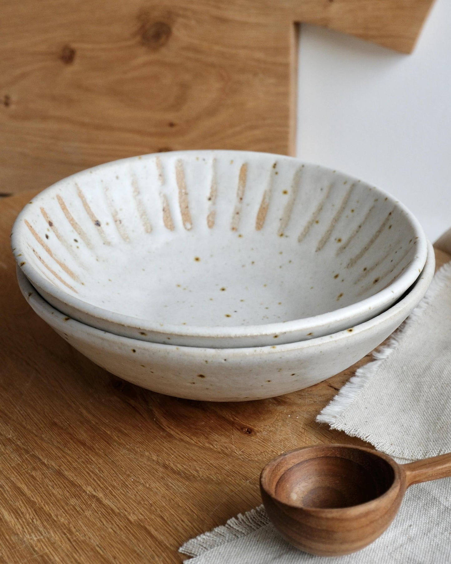 Stack of white ceramic trinket bowls with a wooden spoon on a wooden surface