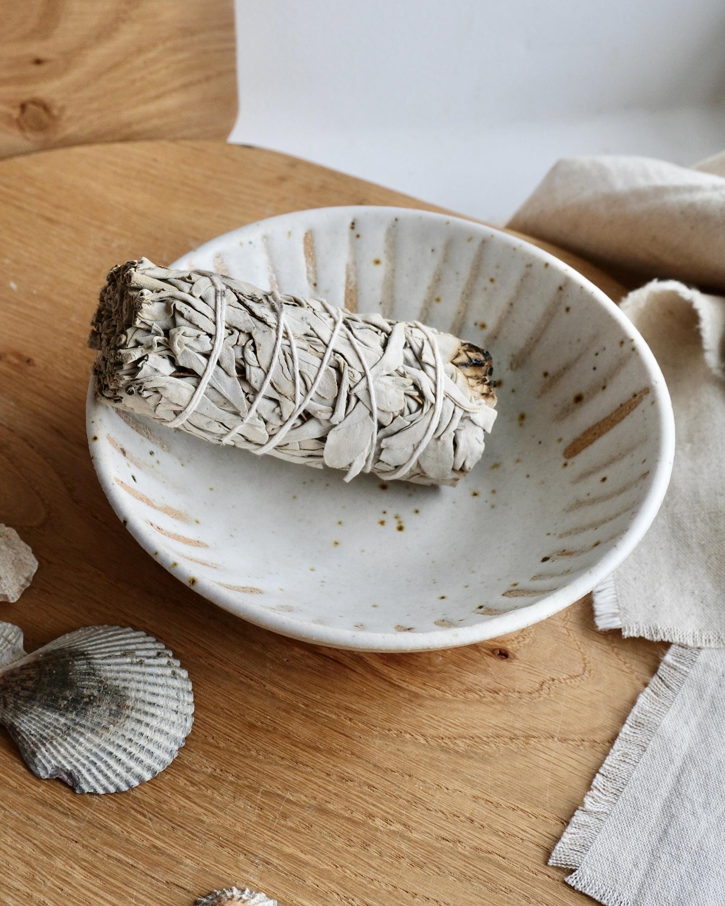 White speckled ceramic bowl with a smouldering sage stick on a wooden surface.