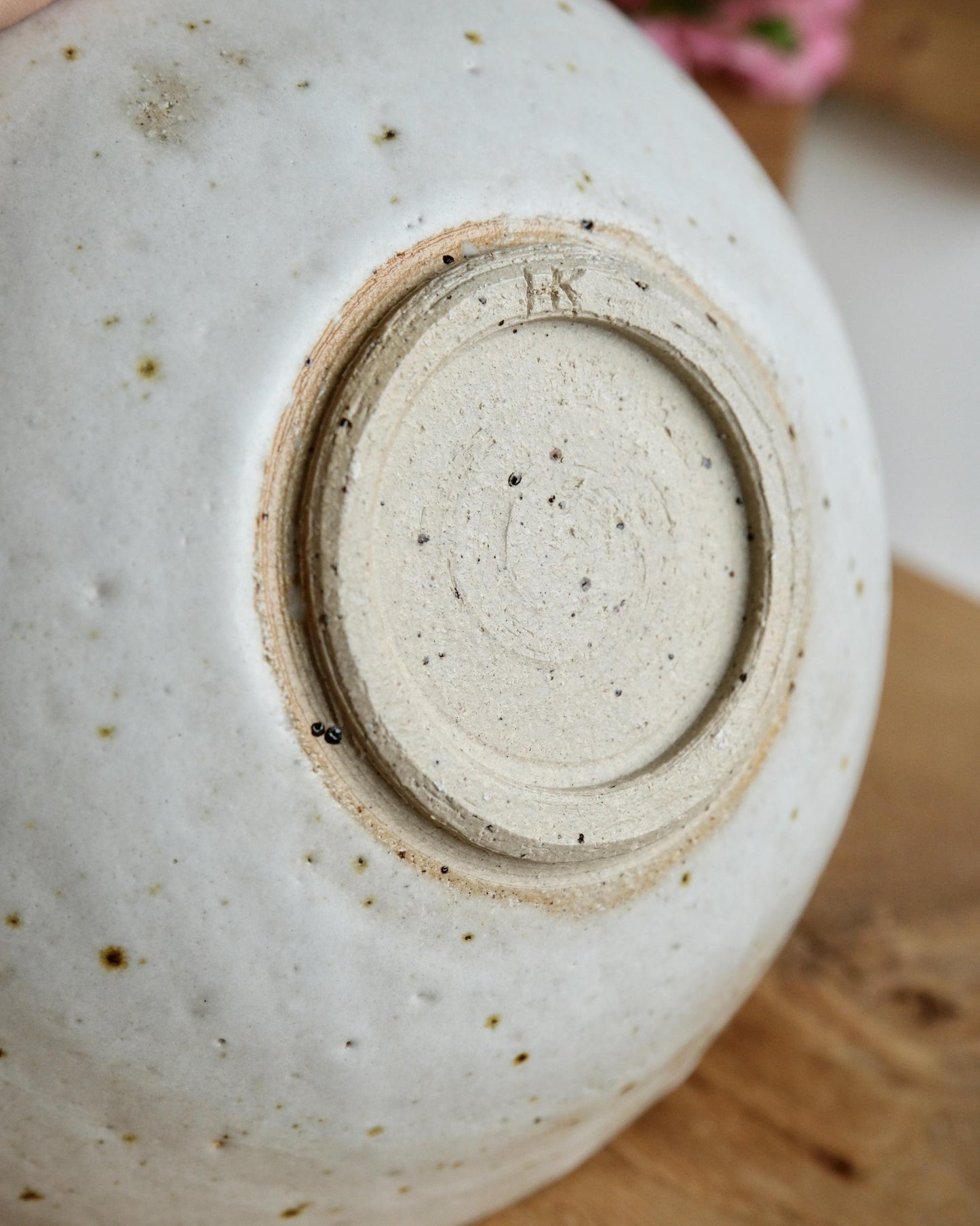 Close-up of a white speckled ceramic trinket dish with a visible brand logo on a wooden surface